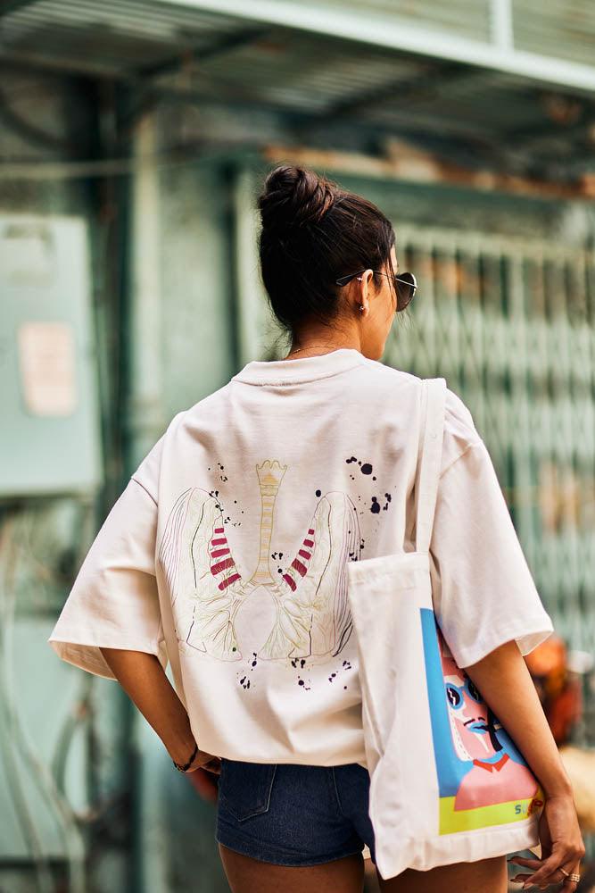 Woman in streetwear style, wearing oversized graphic shirt and carrying printed tote bag