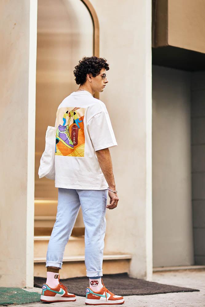 Man in graphic streetwear t-shirt, light blue jeans, and colorful sneakers outdoors