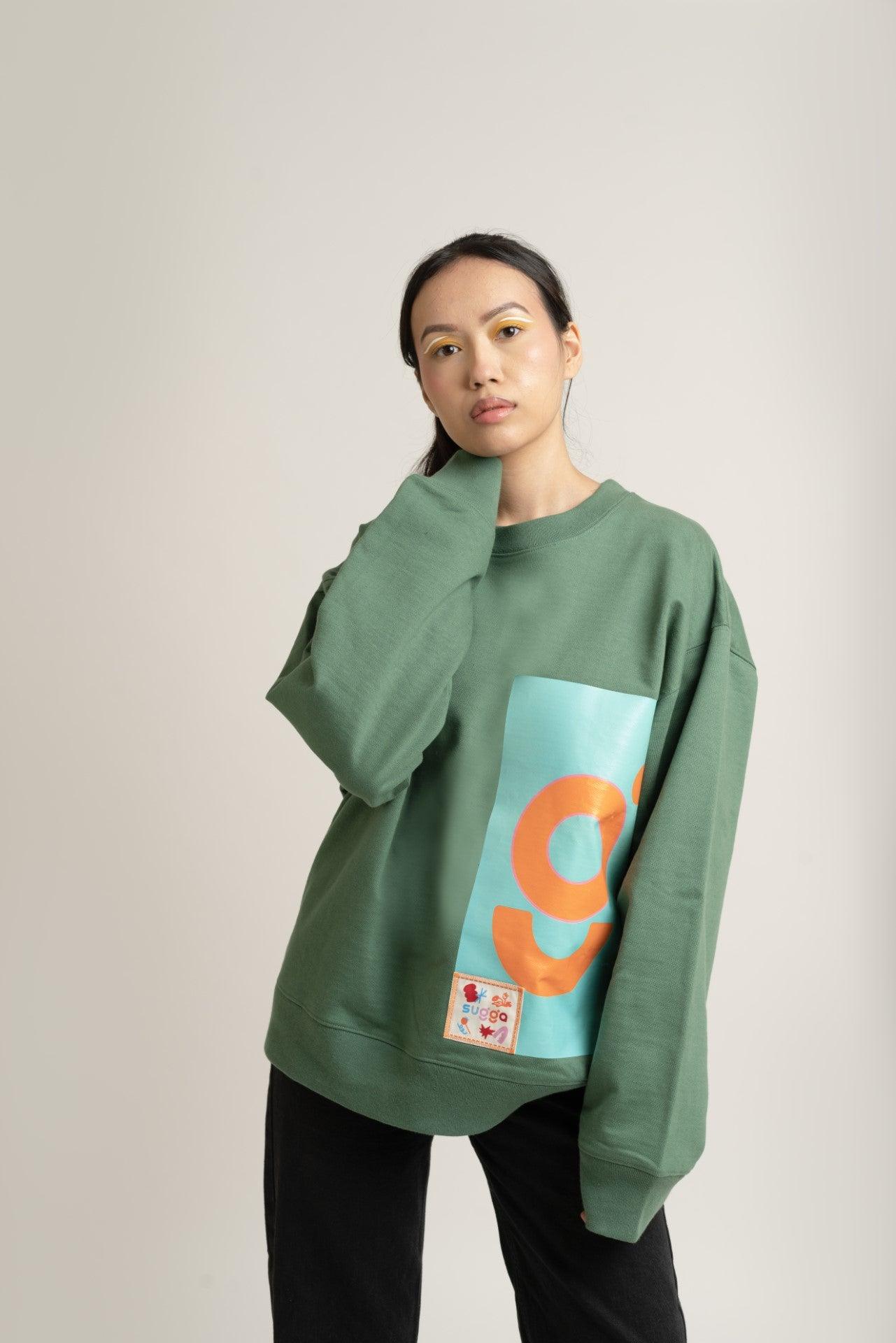 Model in oversized green streetwear sweatshirt with colorful graphic and patch, black pants