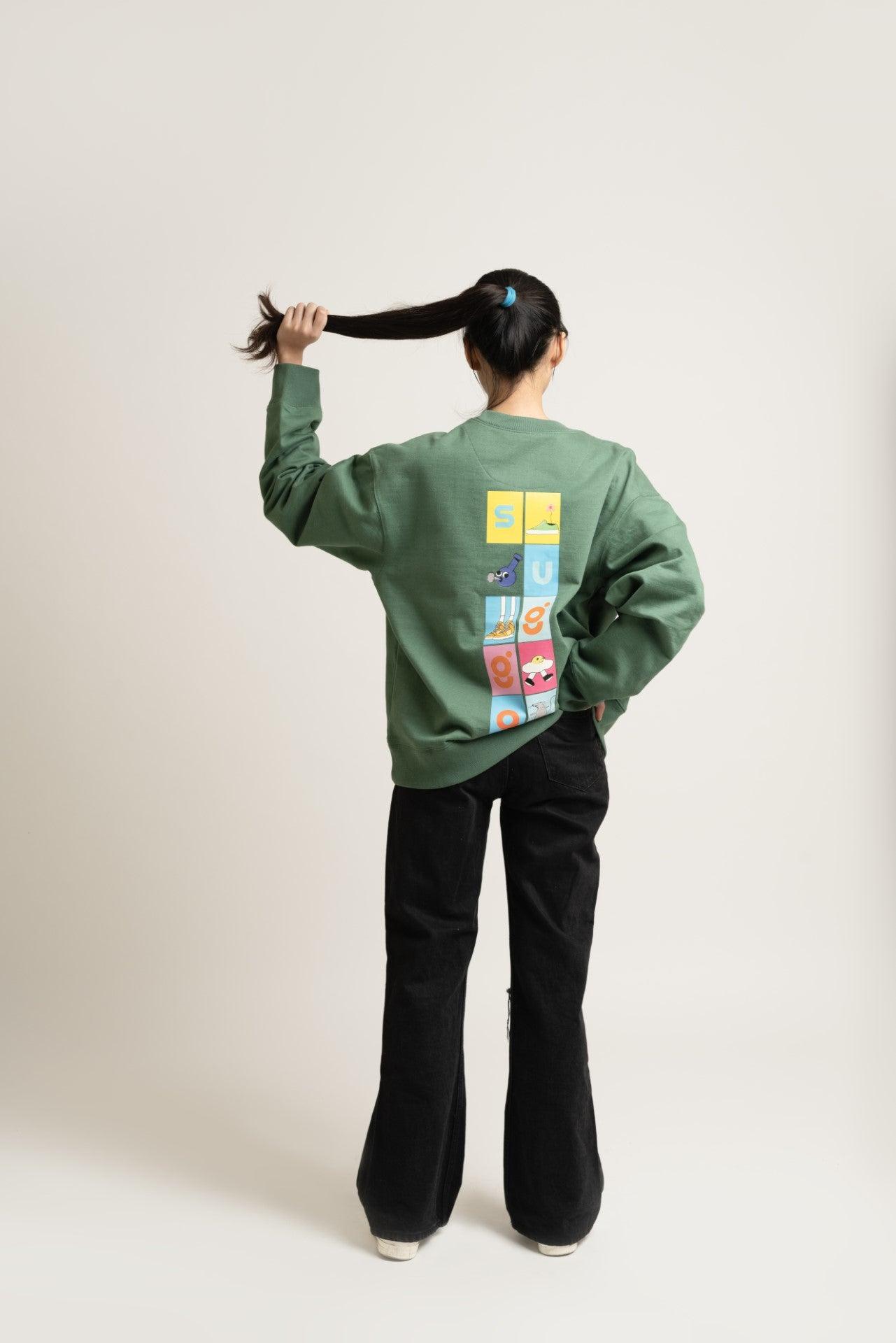 Woman wearing green streetwear sweatshirt with colorful graphic blocks on back, black pants