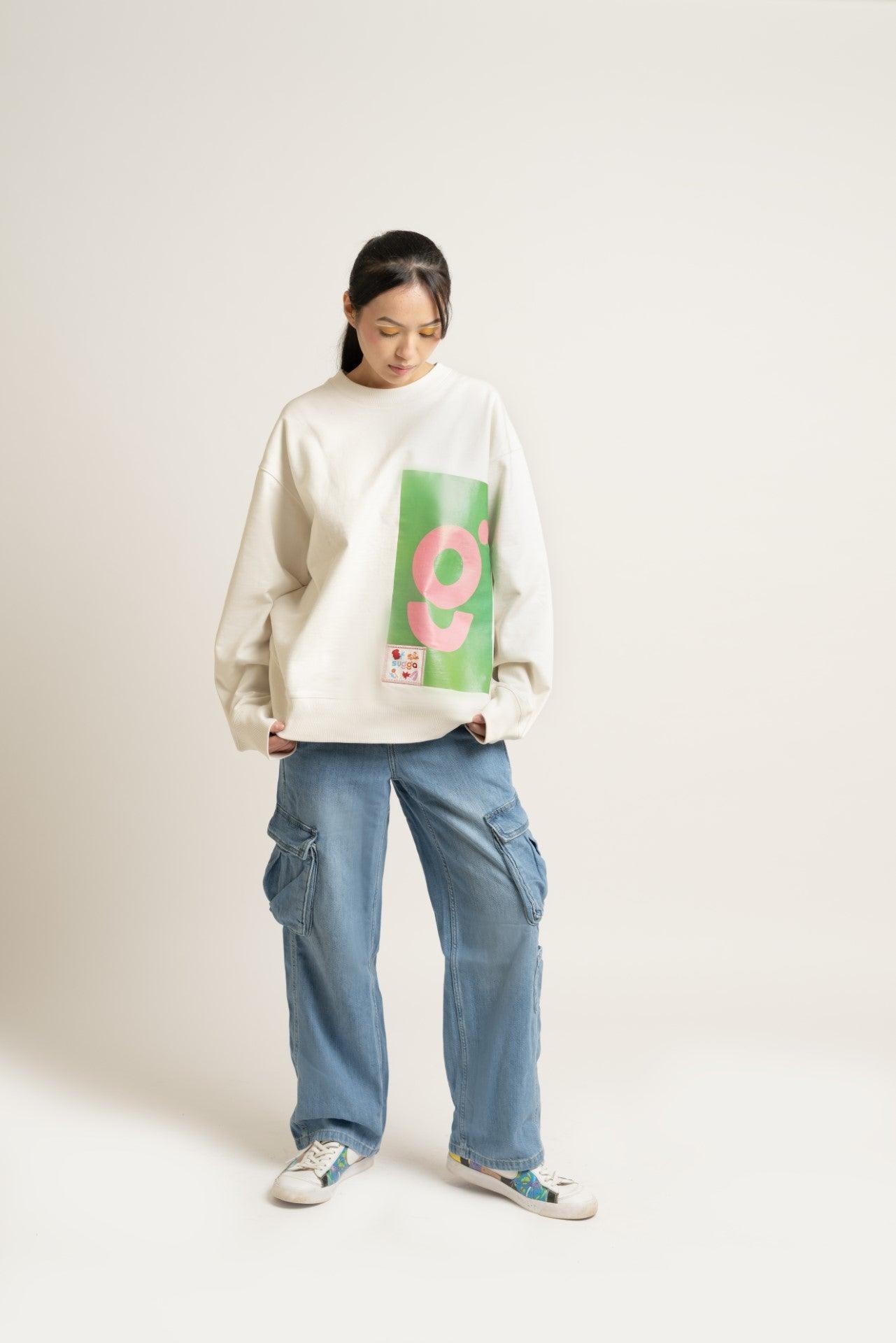 Woman in oversized white graphic sweatshirt with green and pink print, cargo jeans, and sneakers
