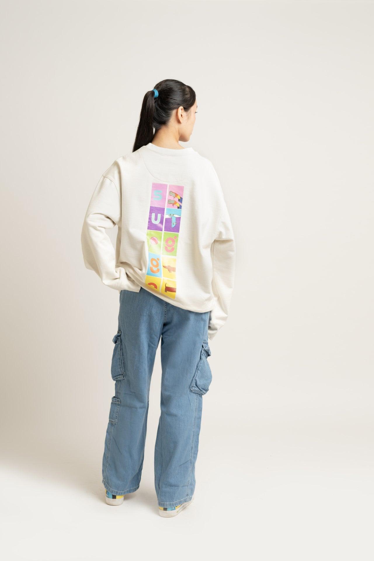 Woman wearing cream graphic sweatshirt with colorful back print and blue cargo jeans