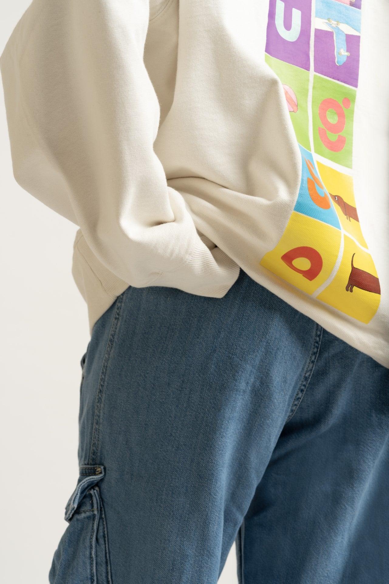 Casual streetwear style with blue cargo jeans and cream graphic sweatshirt