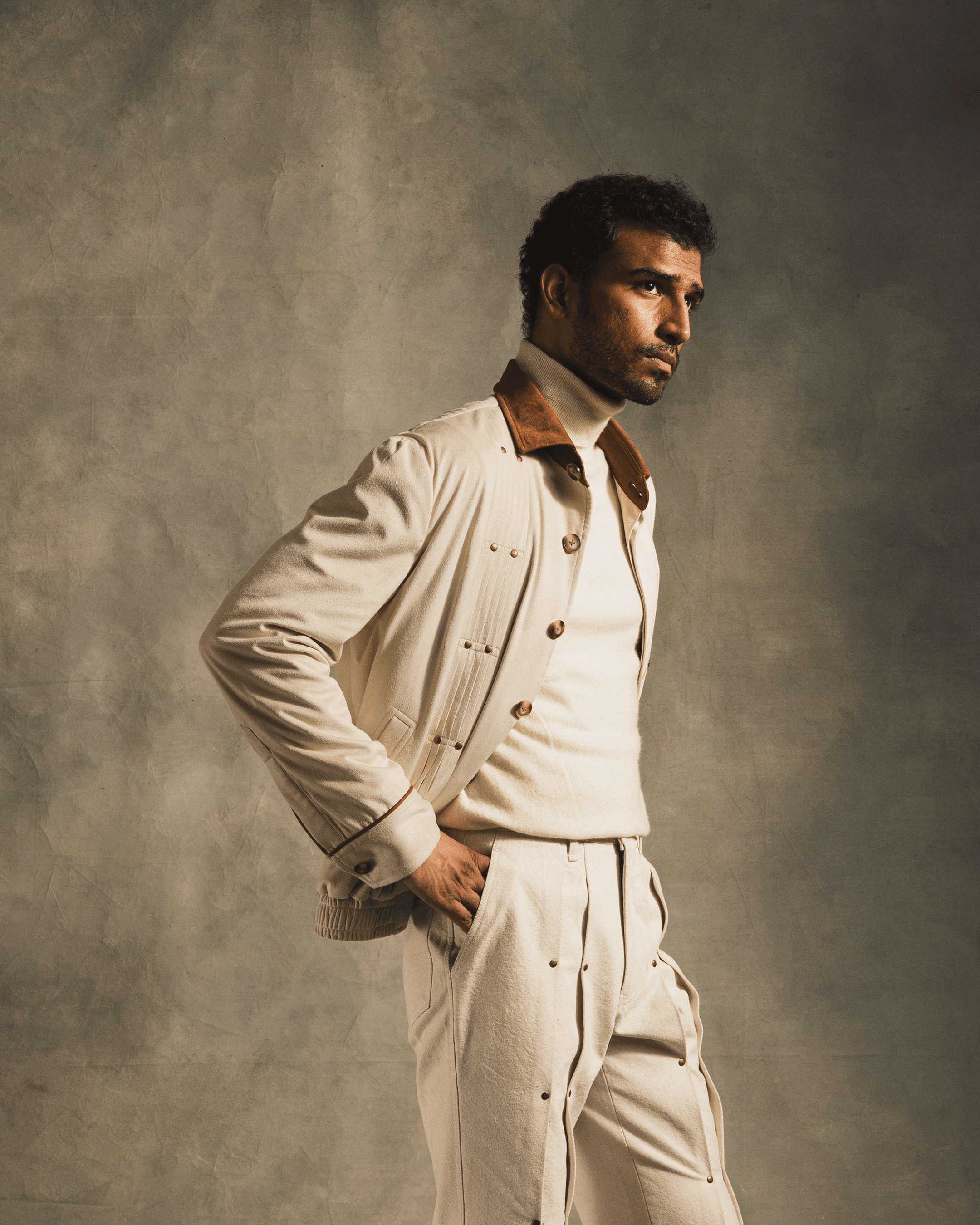 Man wearing beige suede jacket with brown collar, cream turtleneck, and matching pants