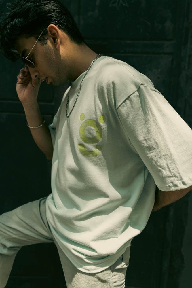 Man wearing oversized graphic streetwear t-shirt with round bear design, sunglasses, necklace