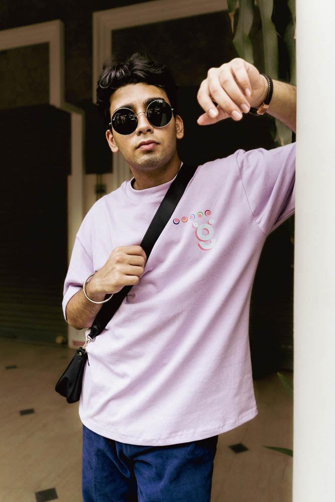 Man in round sunglasses wearing lilac streetwear t-shirt and crossbody bag outdoors