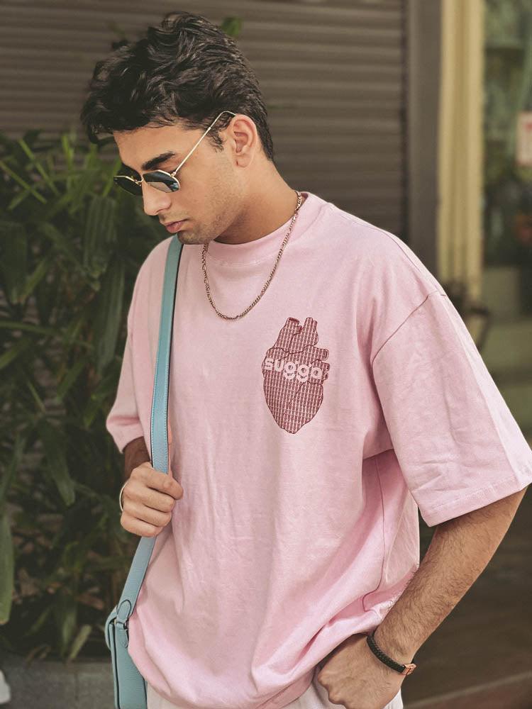 Man wearing a pink streetwear T-shirt with heart graphic, sunglasses, and chain outdoors
