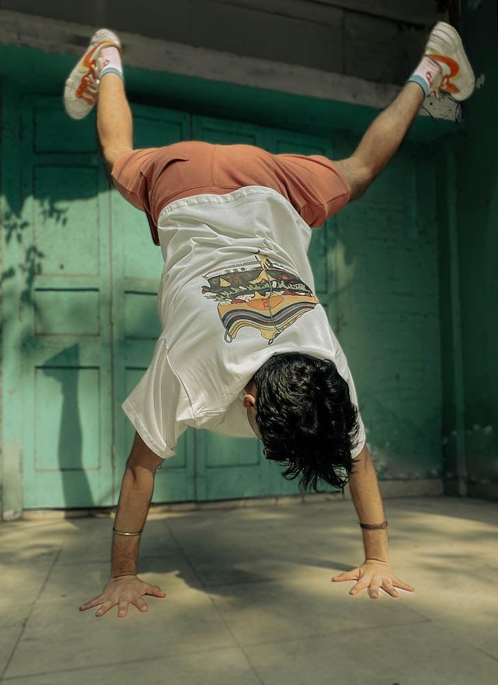 Young man in streetwear t-shirt and shorts doing a handstand outdoors by teal doors
