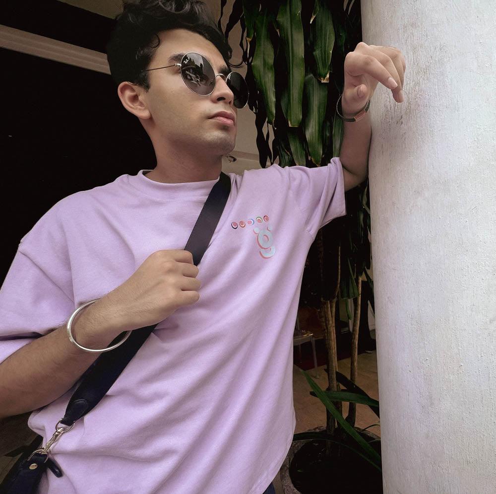 Man in lilac streetwear t-shirt with graphic print, wearing sunglasses, leaning on pillar