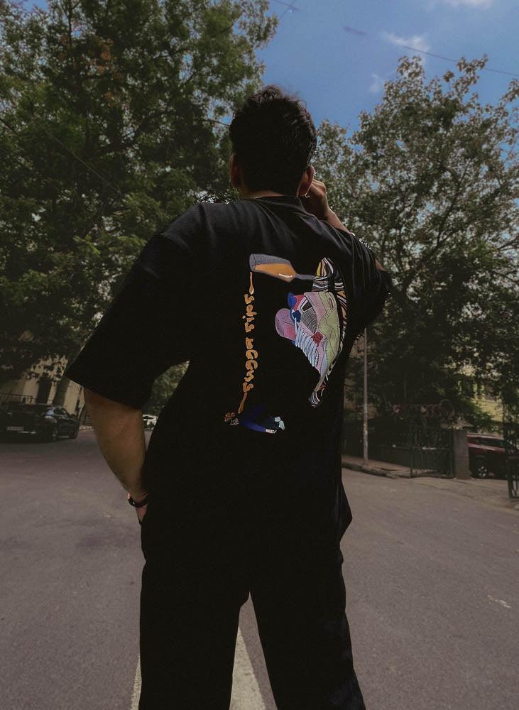 Man wearing black graphic streetwear t-shirt with colorful sneaker design outdoors