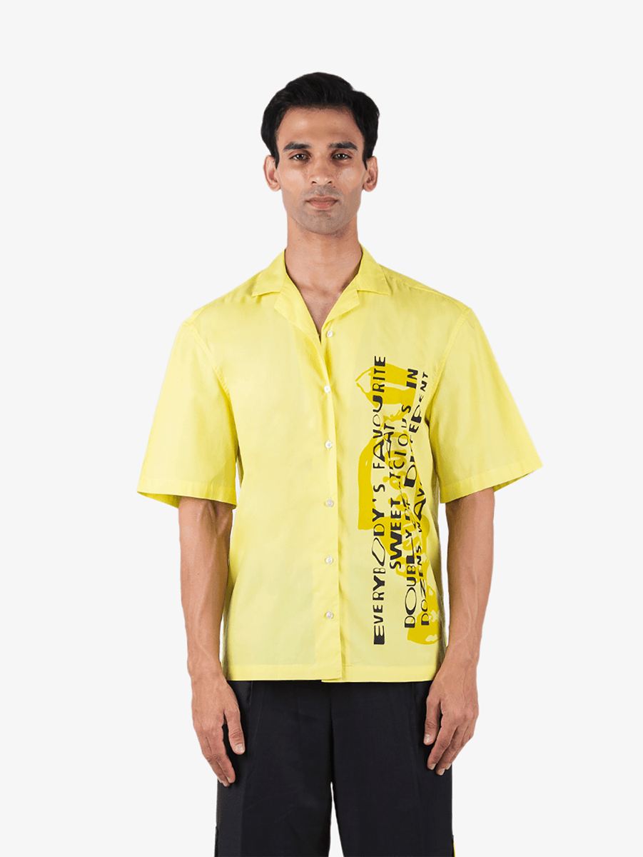 Man wearing a yellow graphic short sleeve button-up shirt with black text print, streetwear style.
