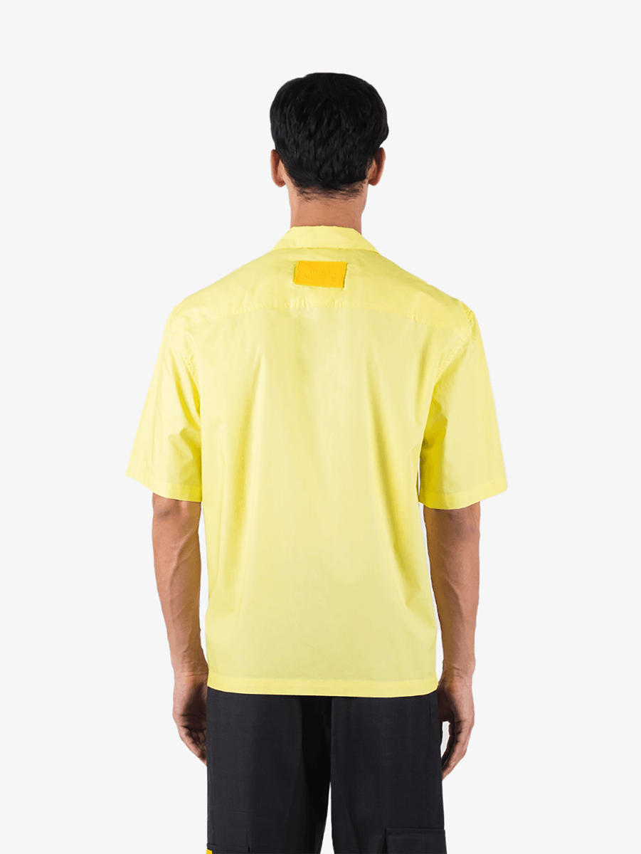 Back view of a man wearing a short-sleeve yellow button-up shirt and black pants