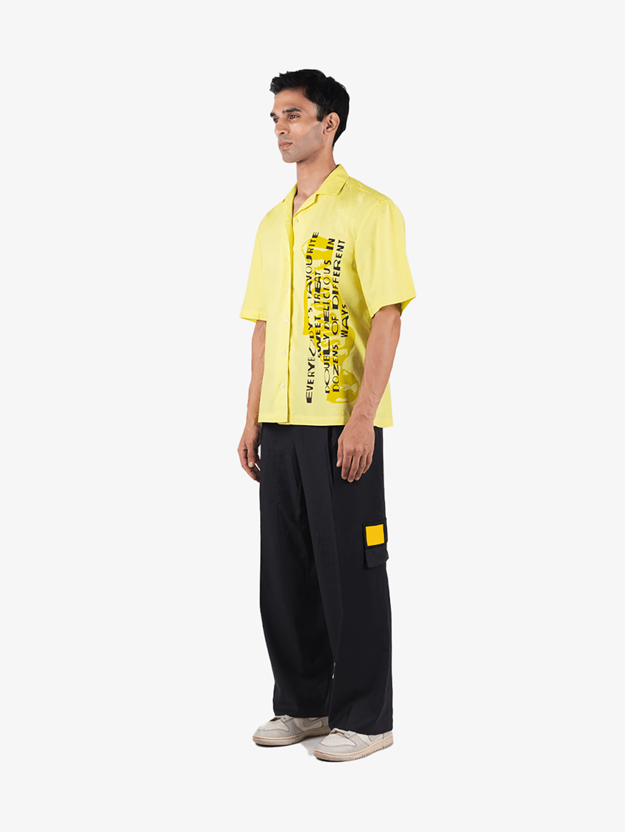 Man modeling yellow graphic short sleeve shirt, black wide-leg cargo pants, white sneakers