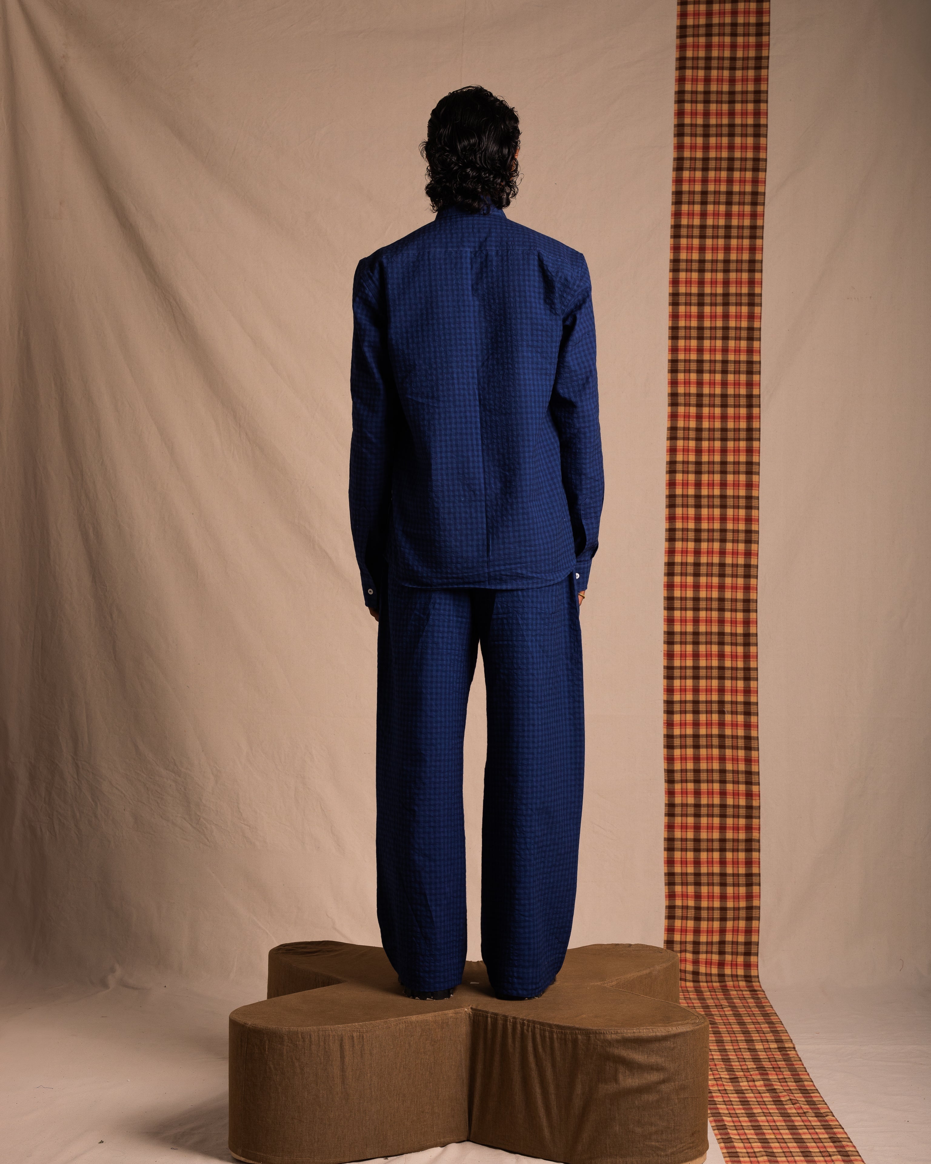 Model in textured blue streetwear suit standing on brown platform, neutral studio backdrop