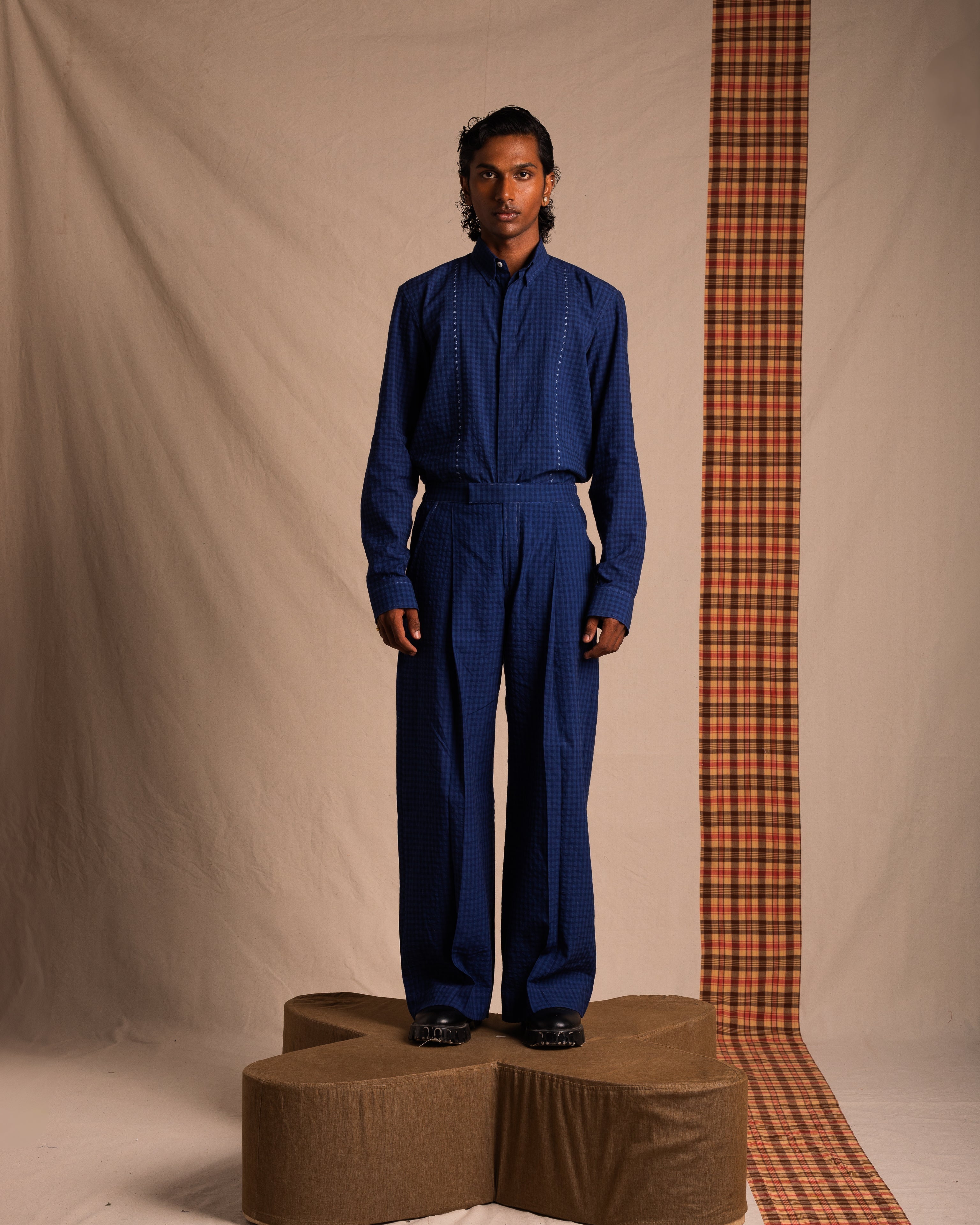 Man wearing blue checkered streetwear set, standing on a pedestal with neutral backdrop