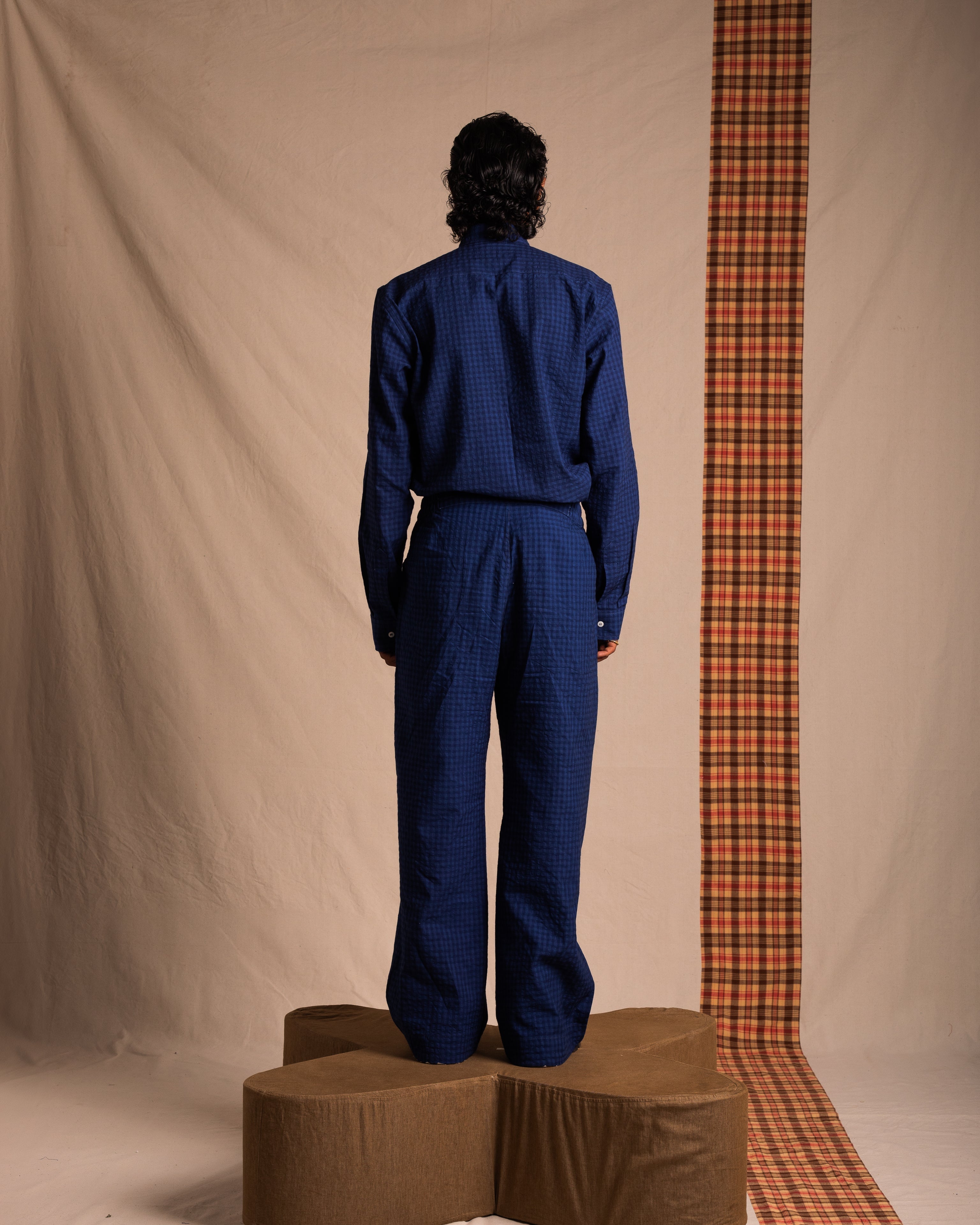 Model in blue checkered streetwear outfit standing on sculpted platform against neutral backdrop