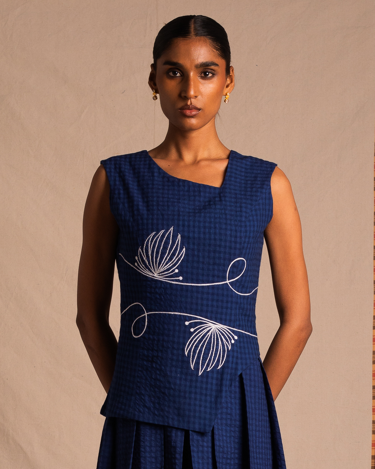 Woman wearing a sleeveless blue textured dress with white floral embroidery, standing indoors