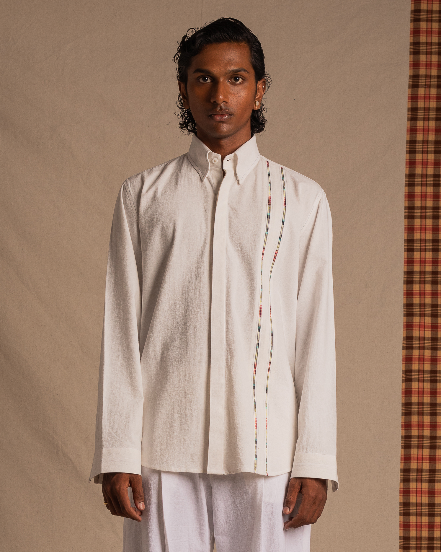 Man wearing a white long sleeve shirt with colored plaid trim, standing against a neutral background