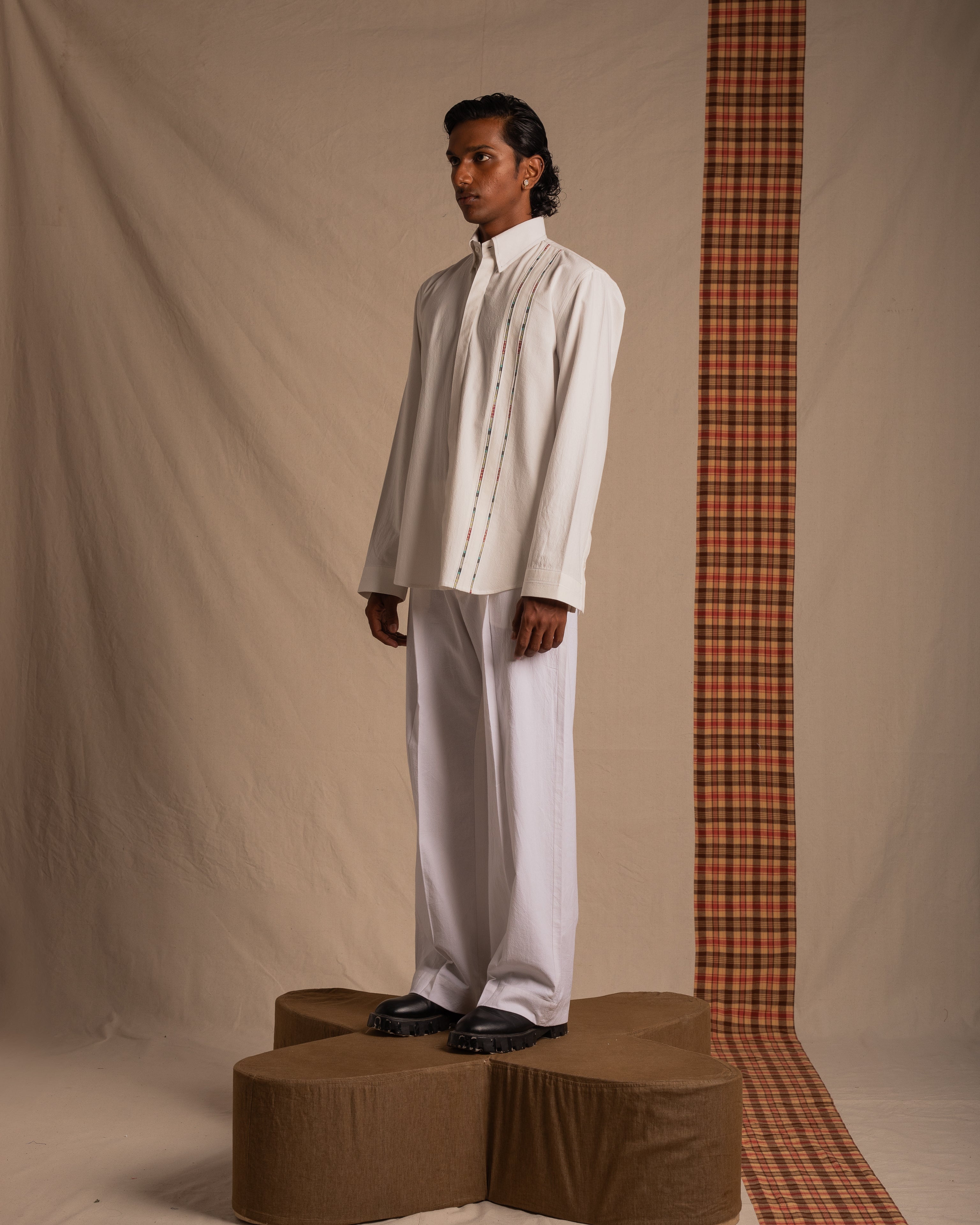 Male model in a modern white streetwear shirt and wide-leg pants, standing on a platform