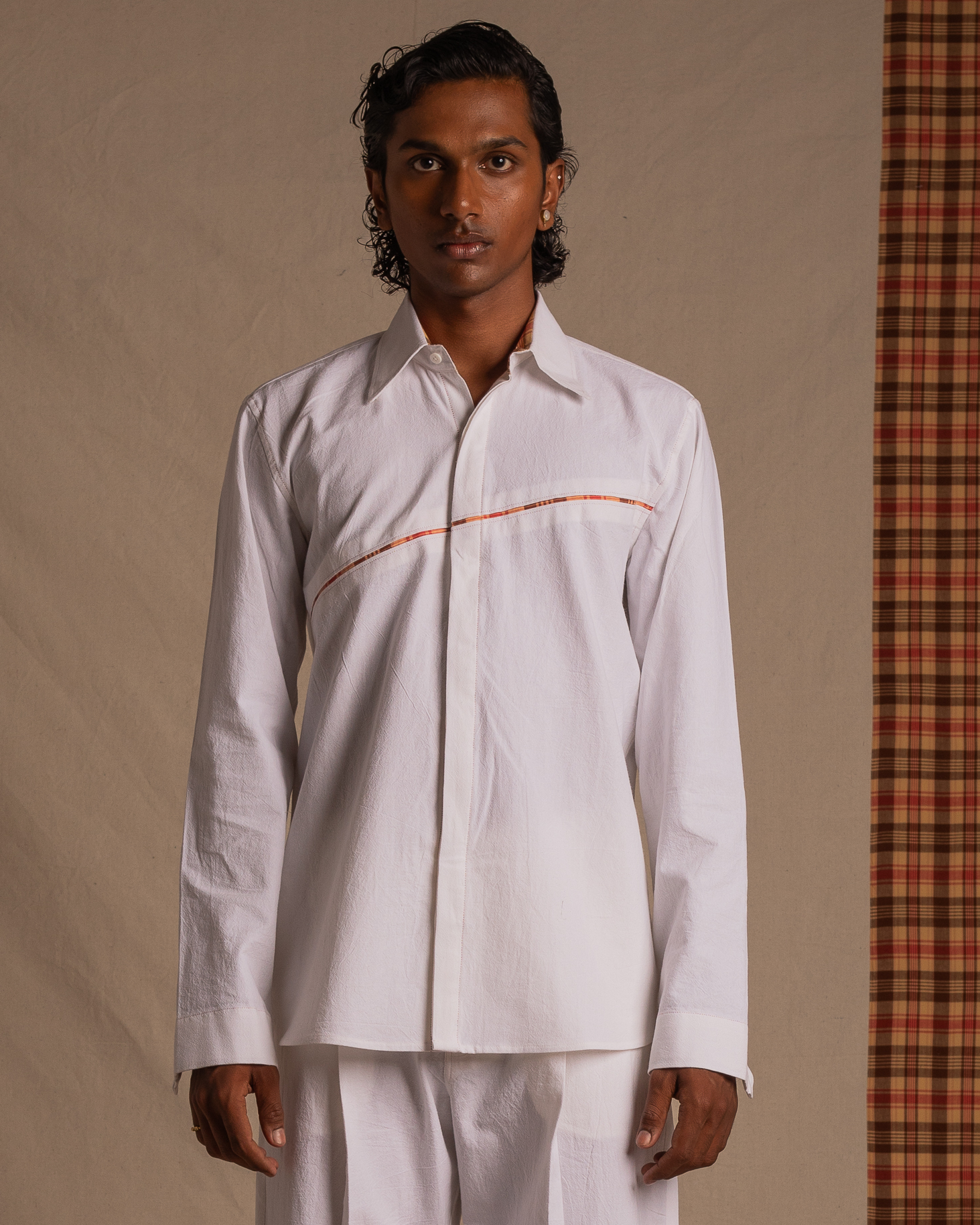 Man wearing a white long sleeve shirt with subtle red accent, standing against a fabric backdrop