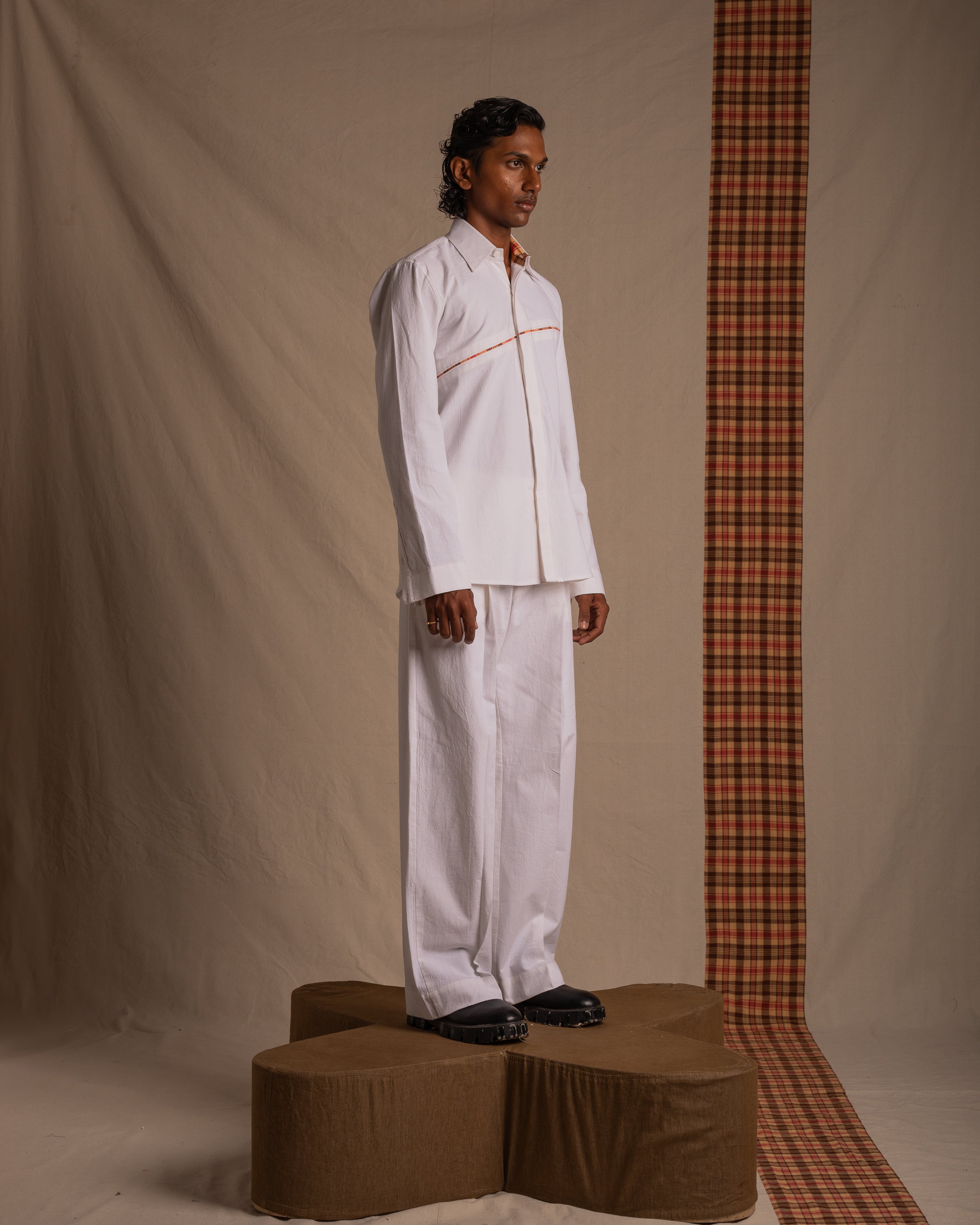 Man modeling white streetwear shirt and pants with black shoes against fabric backdrop