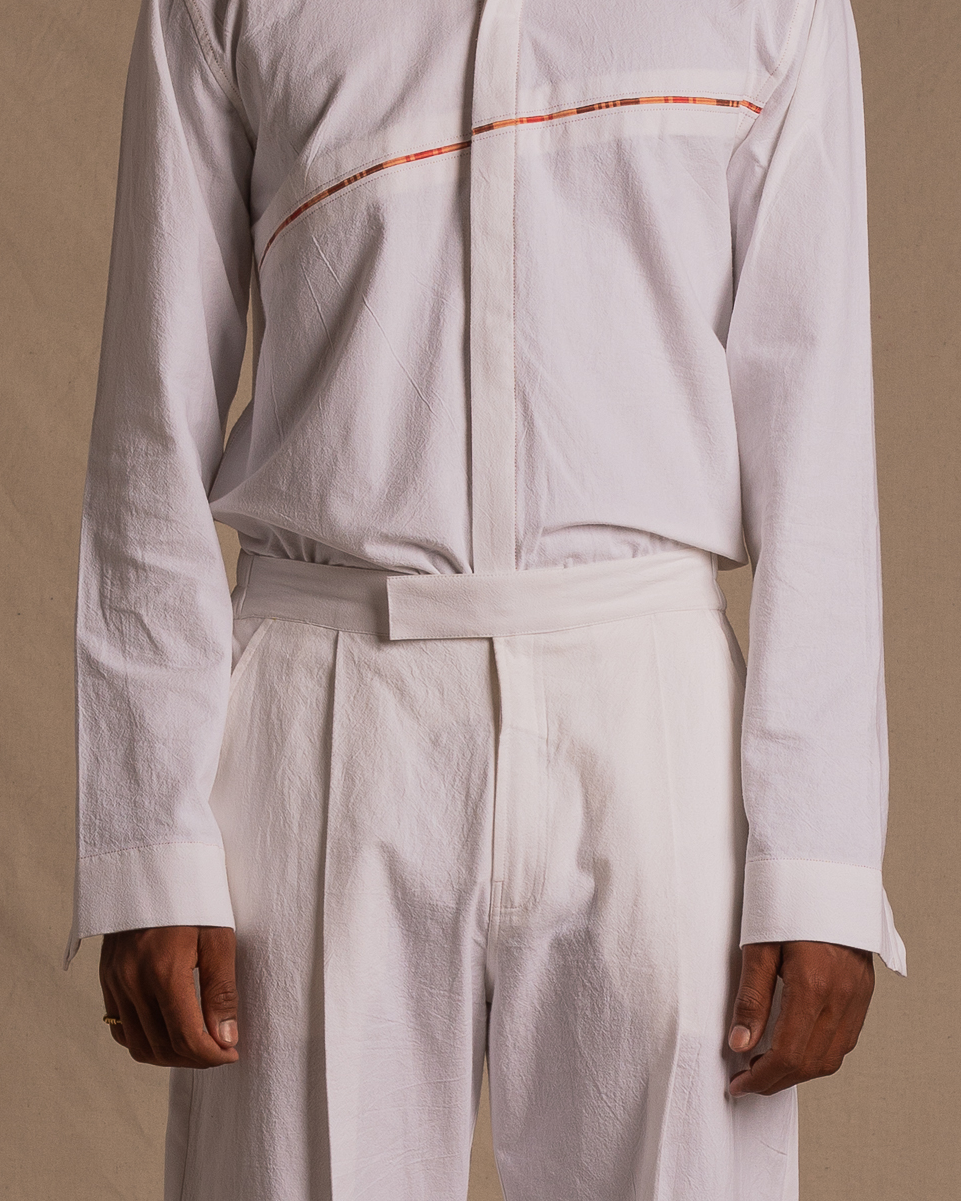 Man wearing white designer shirt with red stripe detail and white tailored pants