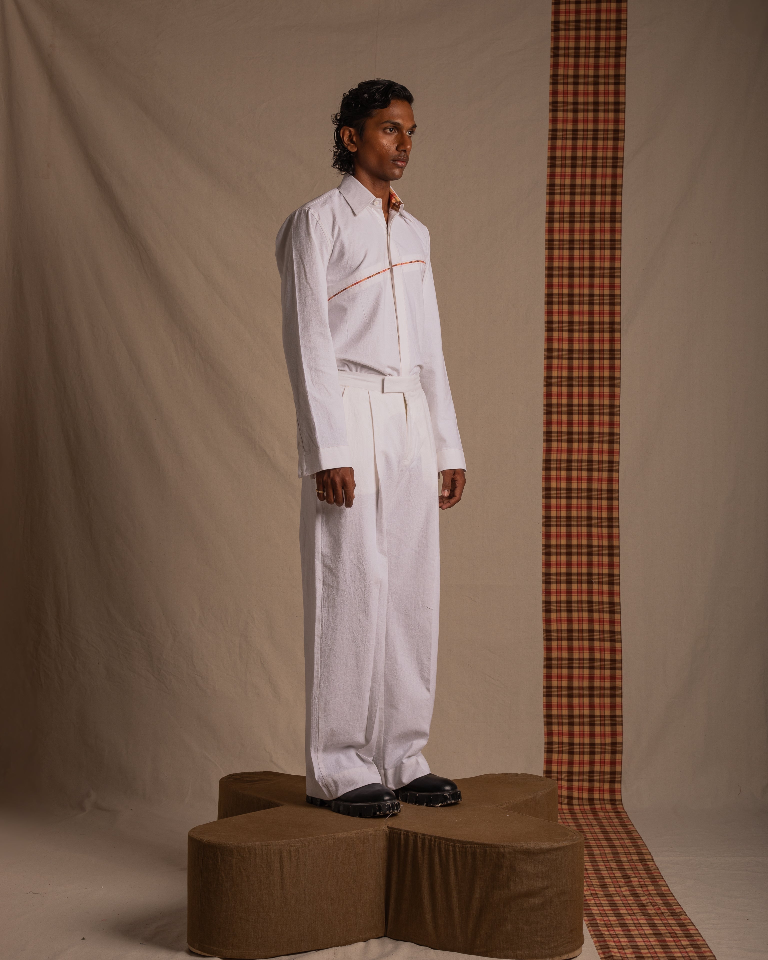 Man modeling streetwear in white button-up shirt and wide-leg pants against neutral backdrop
