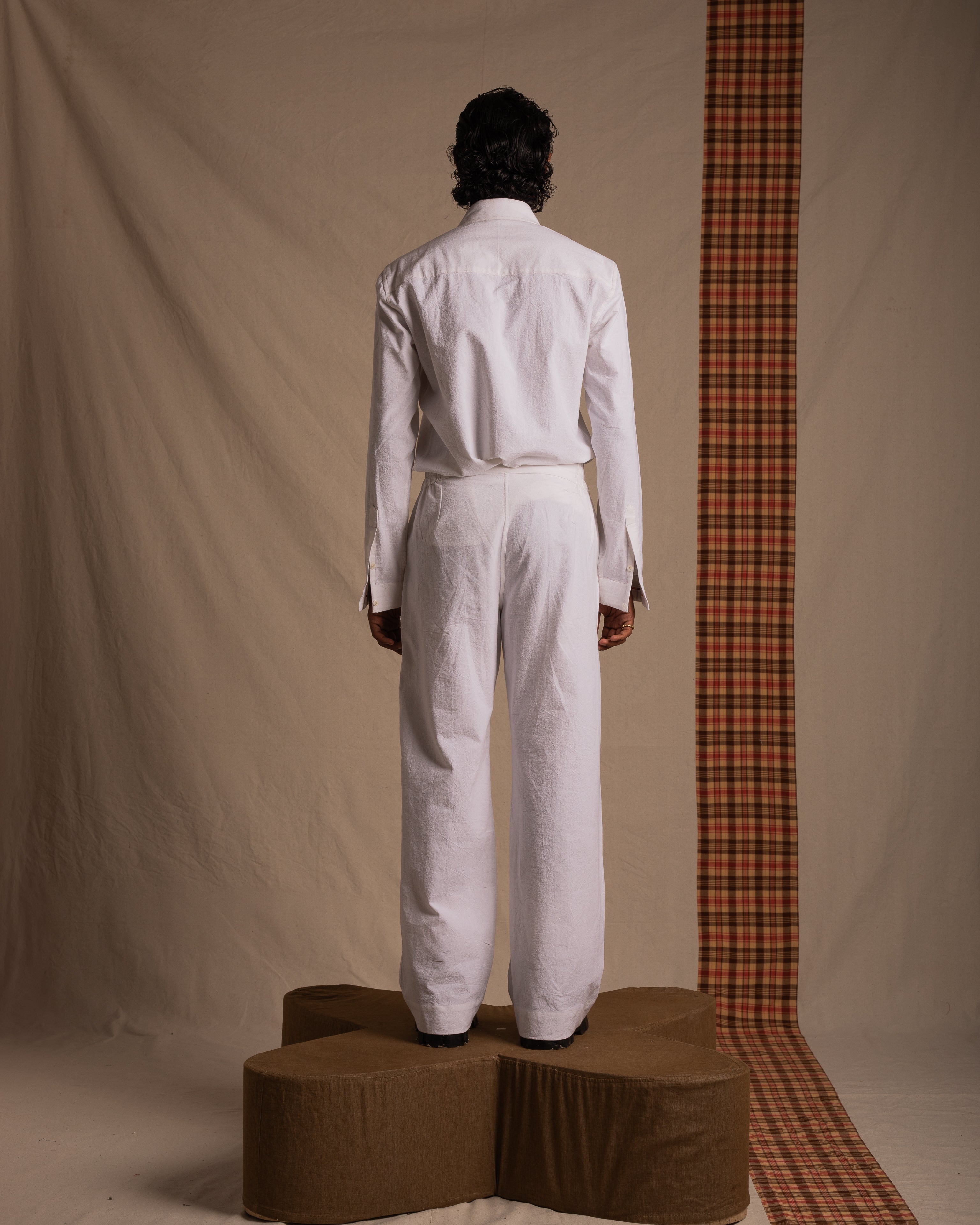 Back view of person in white shirt and pants standing on abstract platform, neutral backdrop