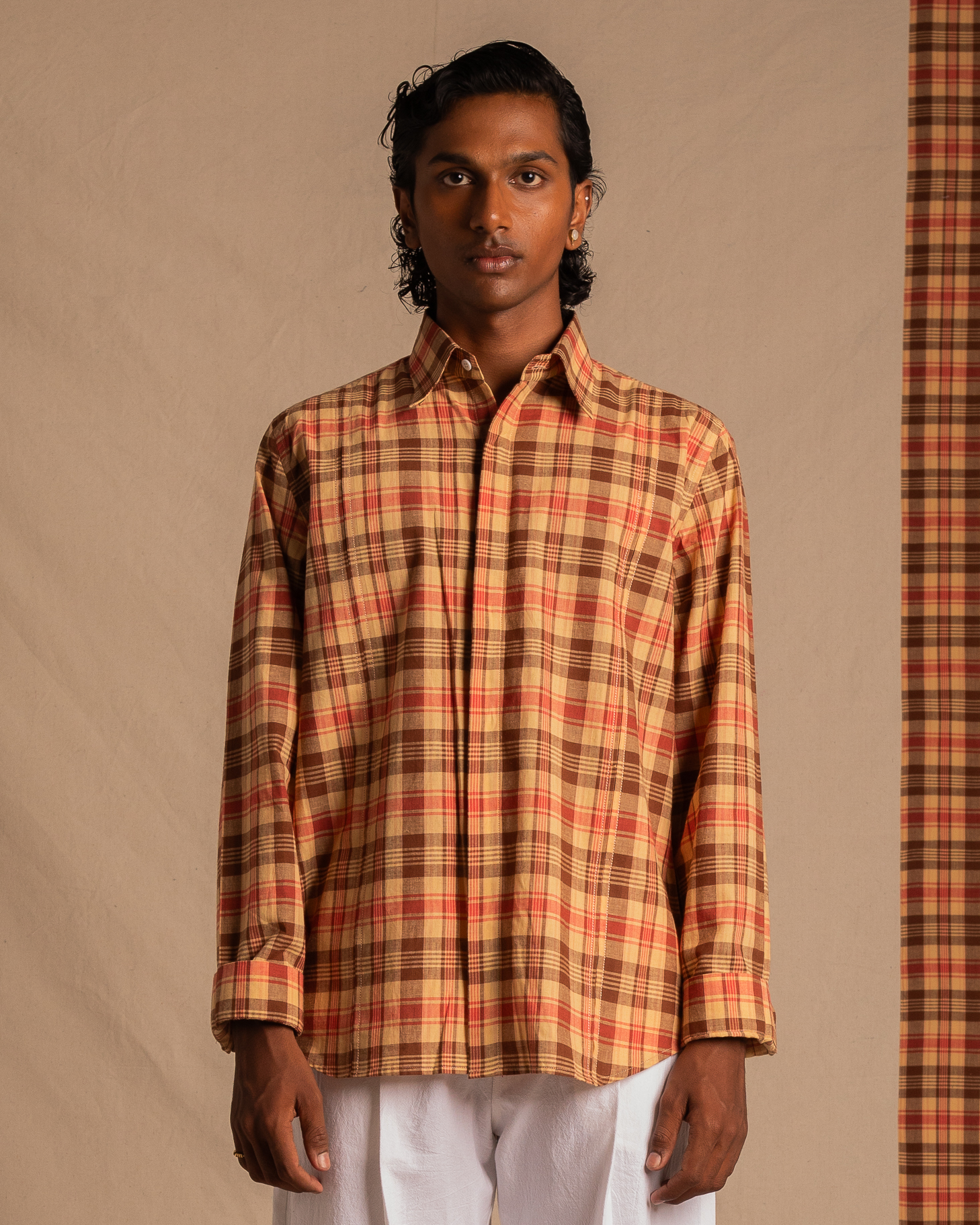Man wearing long sleeve orange and brown plaid shirt with white pants, neutral background
