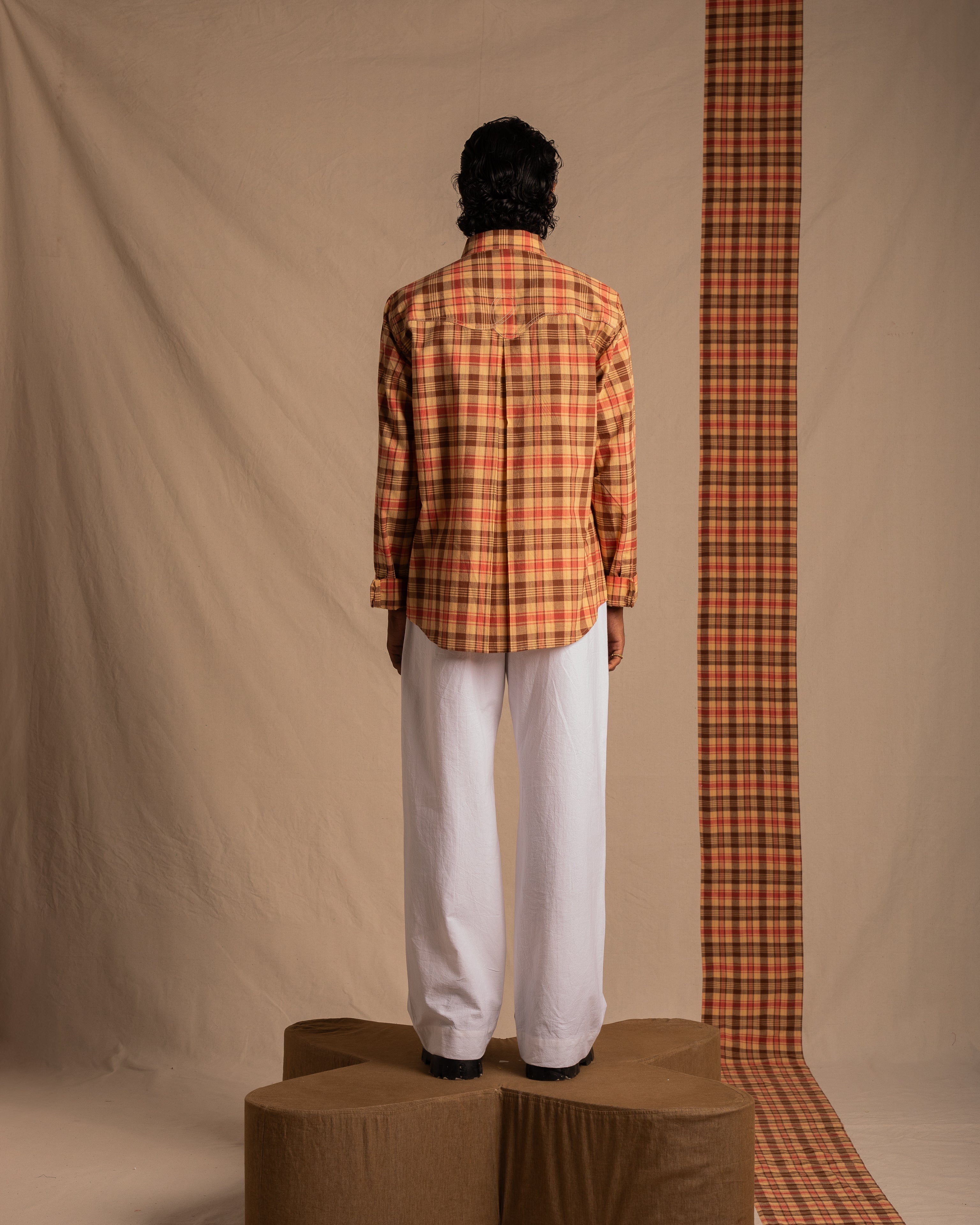 Man modeling yellow and red plaid shirt with white pants against beige backdrop