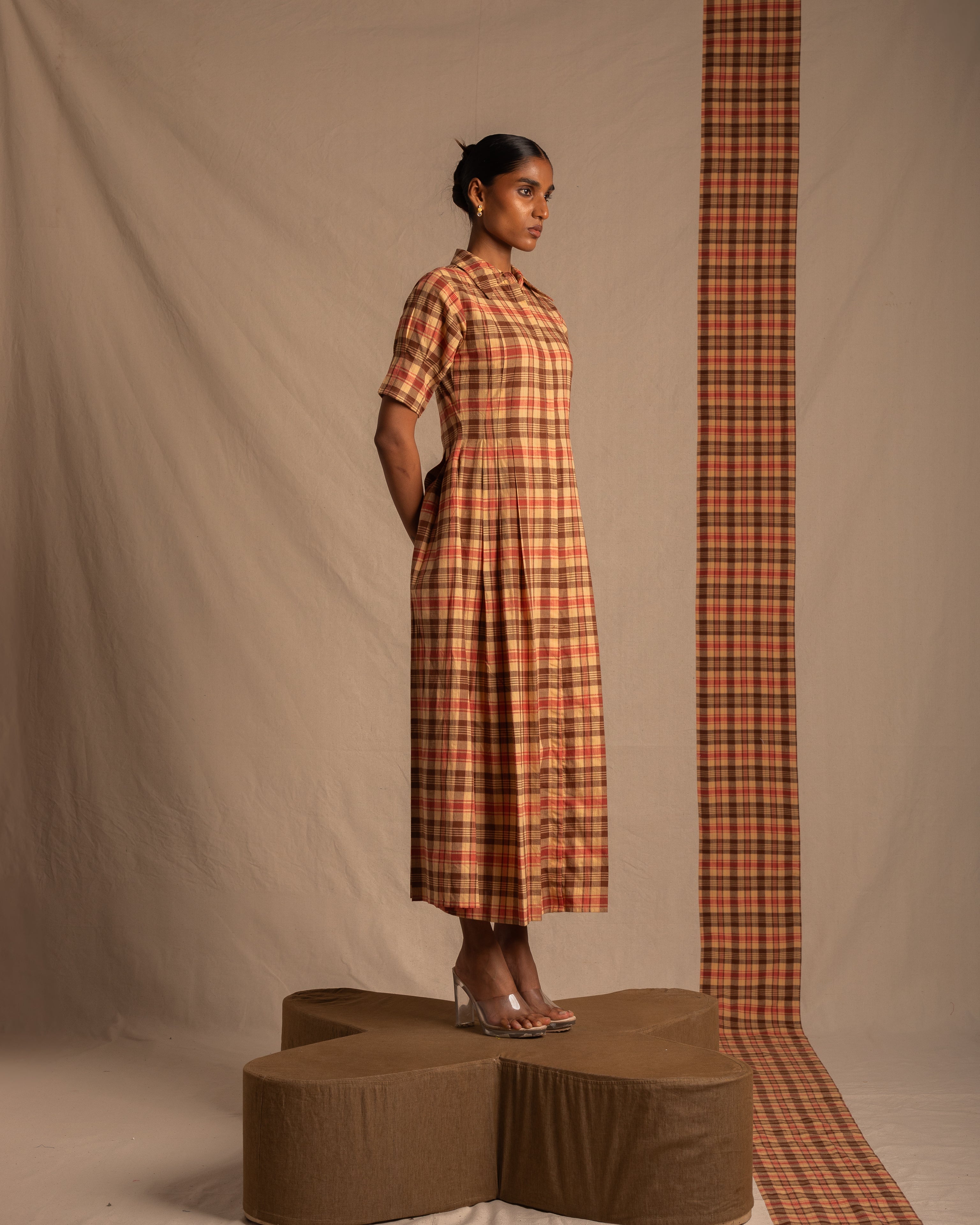 Woman in a brown and red plaid midi dress with short sleeves, clear heels, standing on a fabric platform in a studio setting.