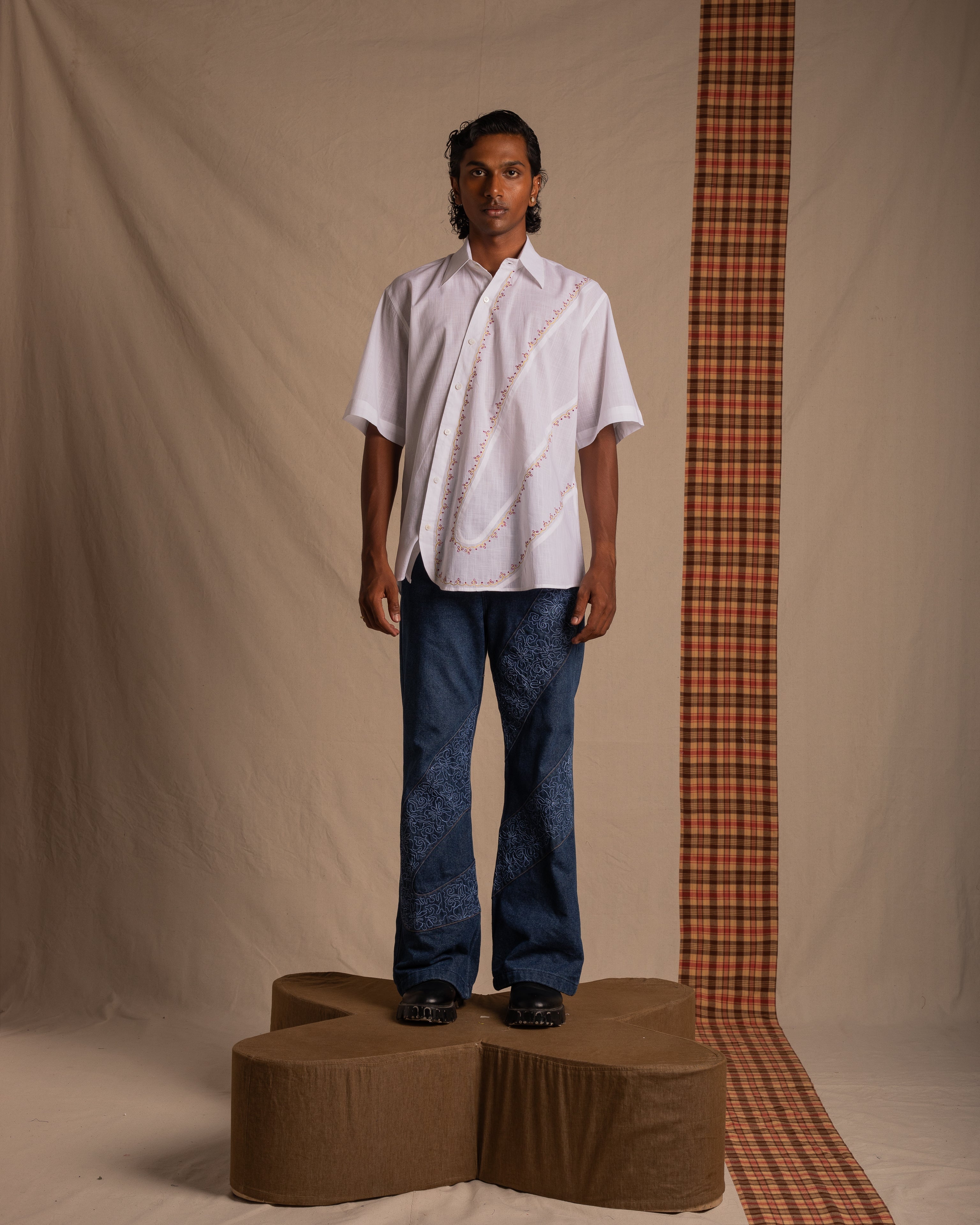 Man in a white short sleeve shirt and patterned blue jeans standing on a brown platform.