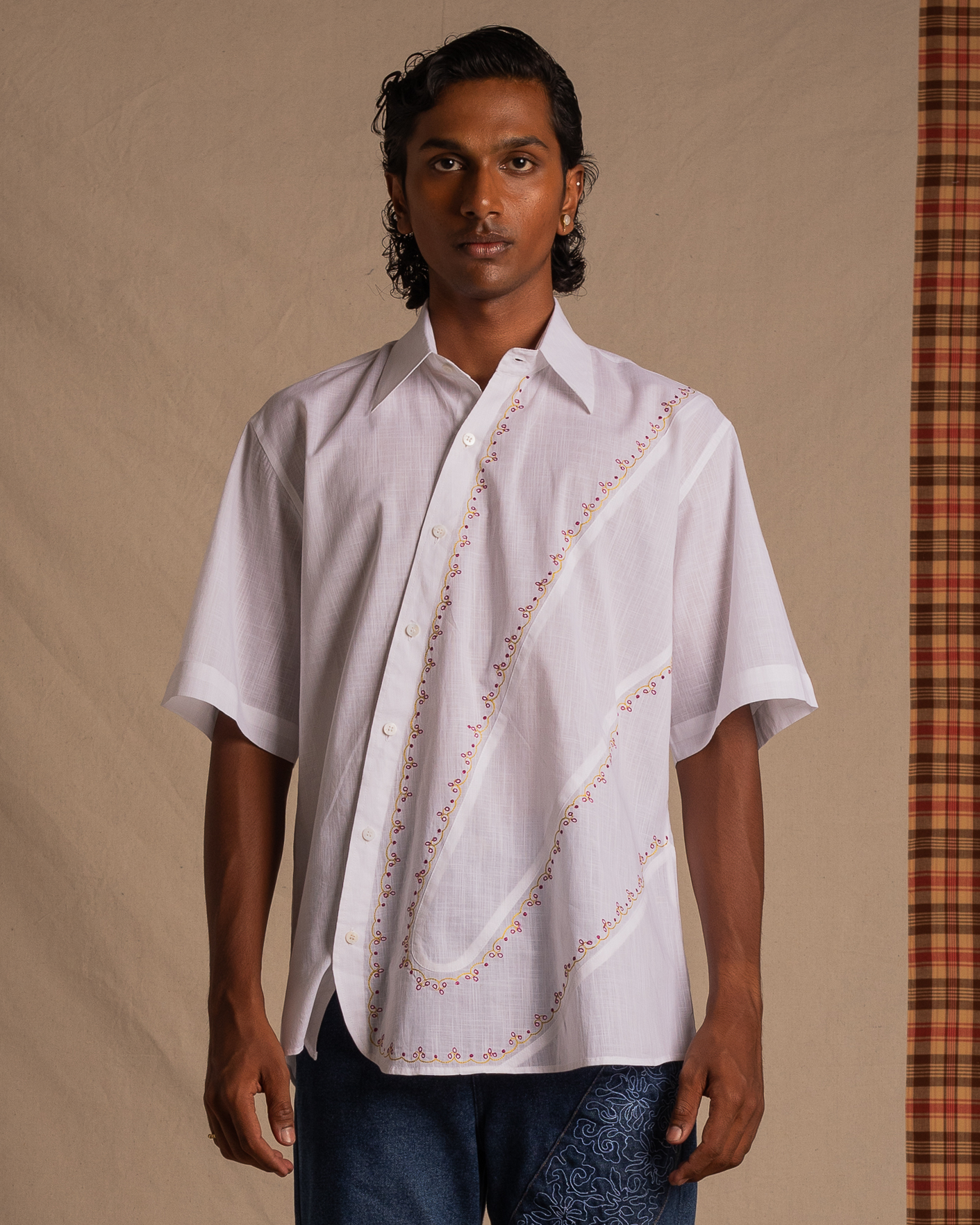 Man modeling a white short-sleeve embroidered shirt with relaxed fit, modern streetwear style