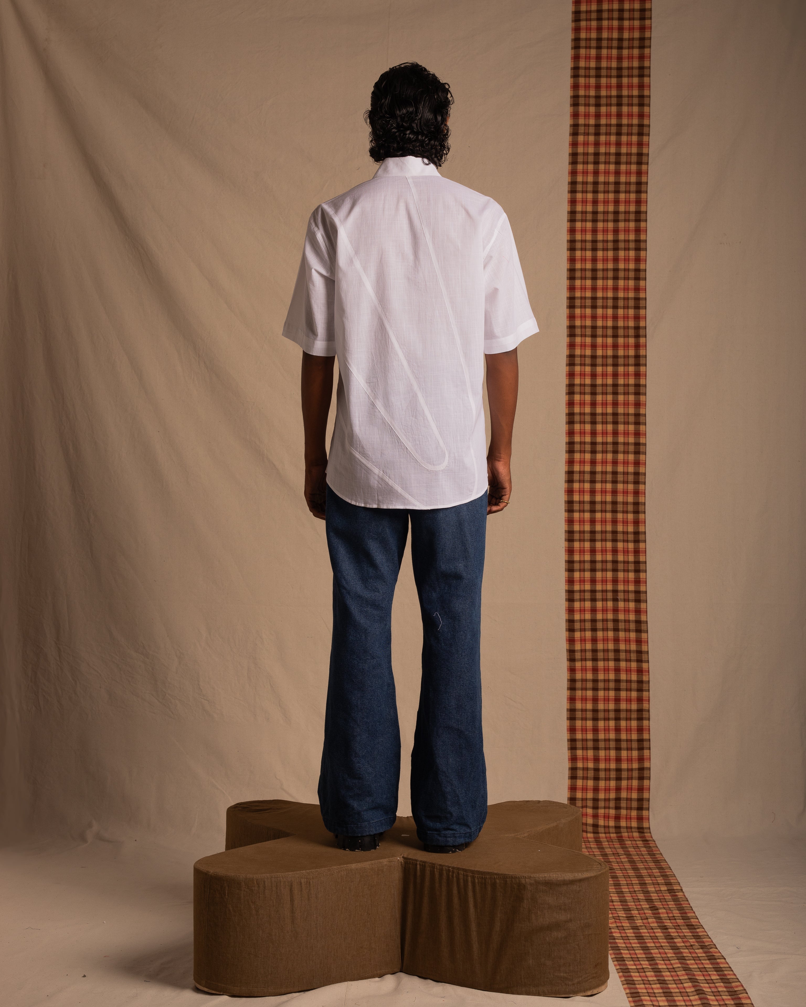 Man in white short sleeve shirt and wide-leg jeans standing on platform, neutral studio backdrop