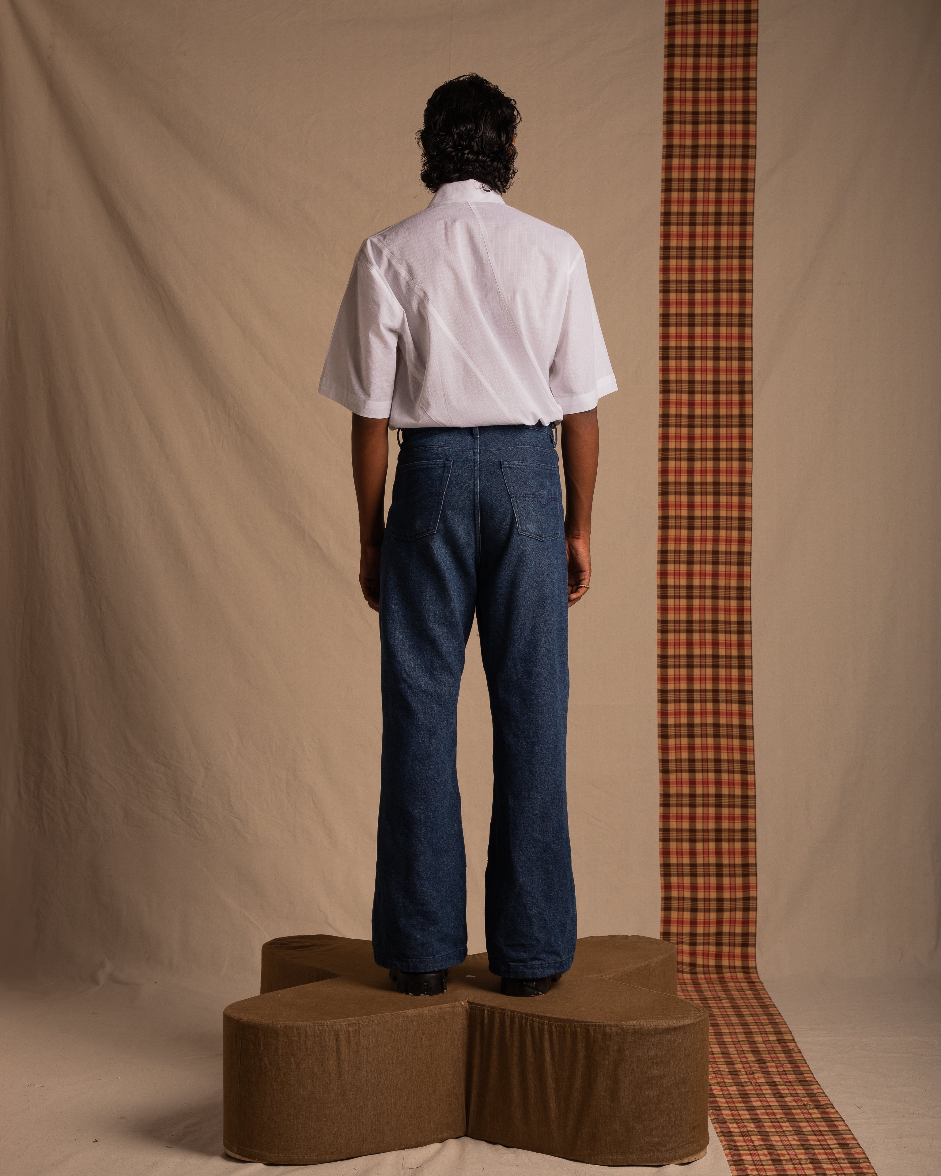 Man modeling casual streetwear with a white short sleeve shirt and wide-leg blue jeans