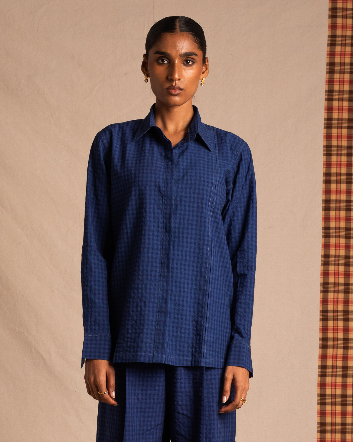 Woman wearing a blue checkered button-up shirt and matching pants, standing indoors.