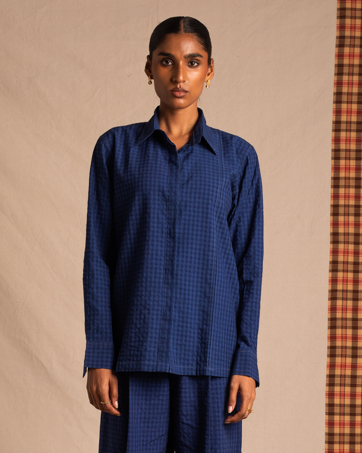 Woman wearing a blue checkered long-sleeve shirt and matching pants, minimal background
