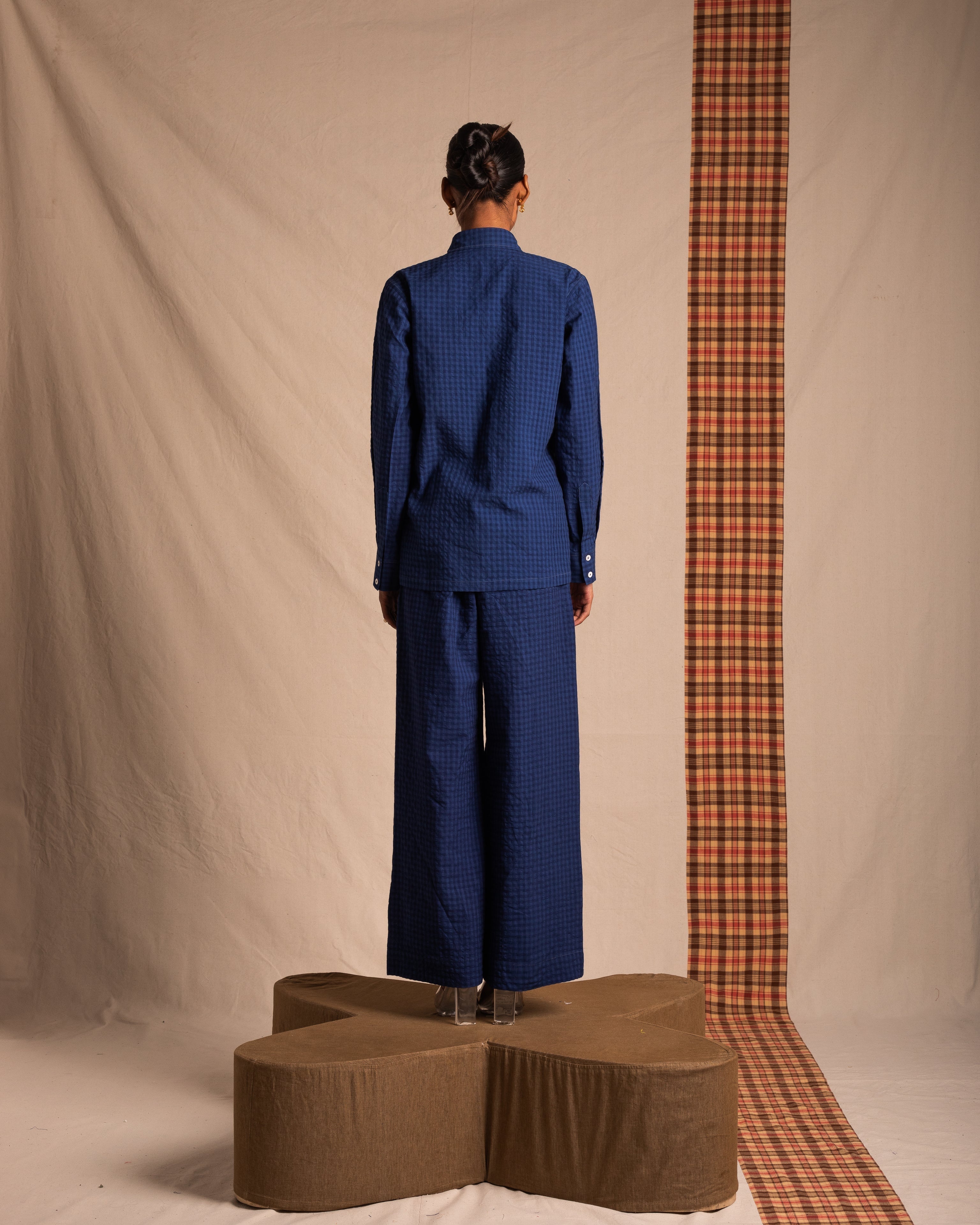 Person wearing a blue checkered shirt and wide-leg pants, standing on a platform indoors