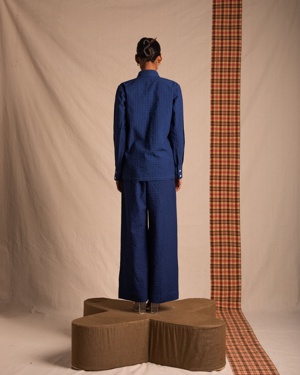 Person wearing a blue checkered shirt and wide-leg pants, standing on a platform indoors