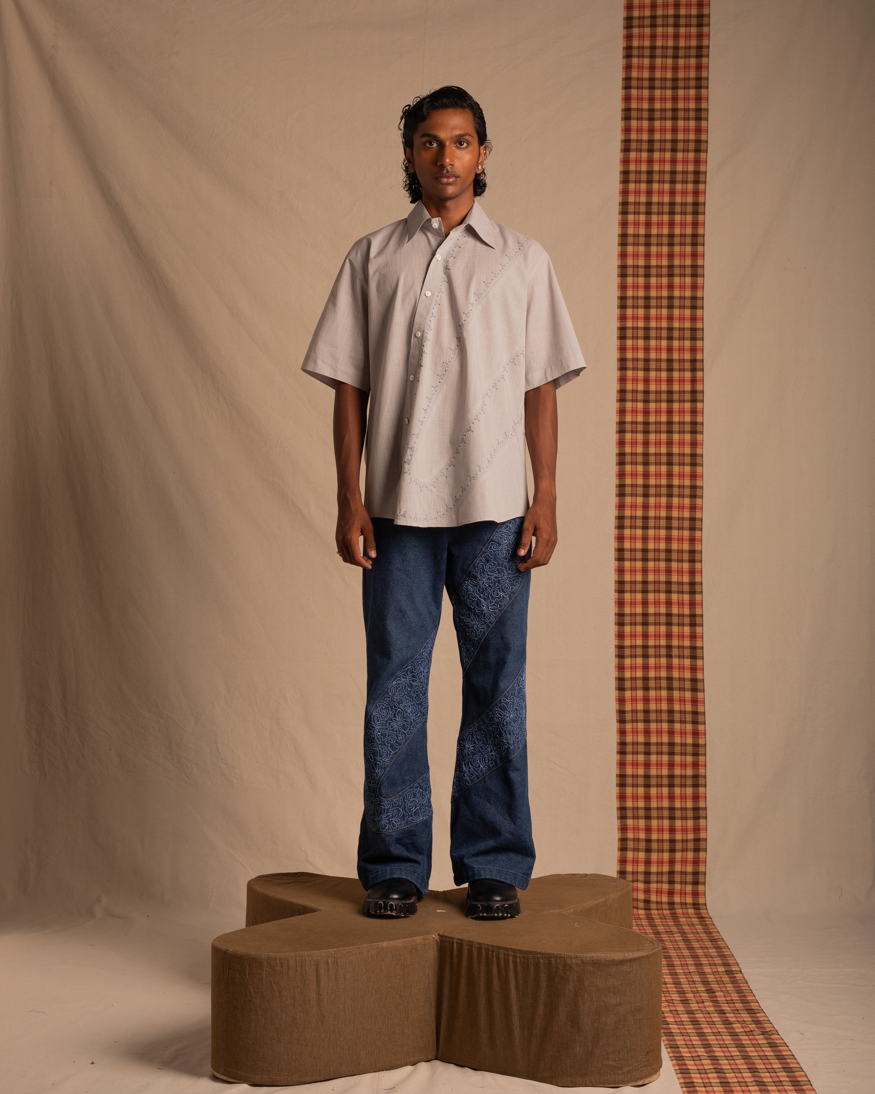 Man modeling a light short-sleeve shirt and blue patterned jeans in a minimalist studio