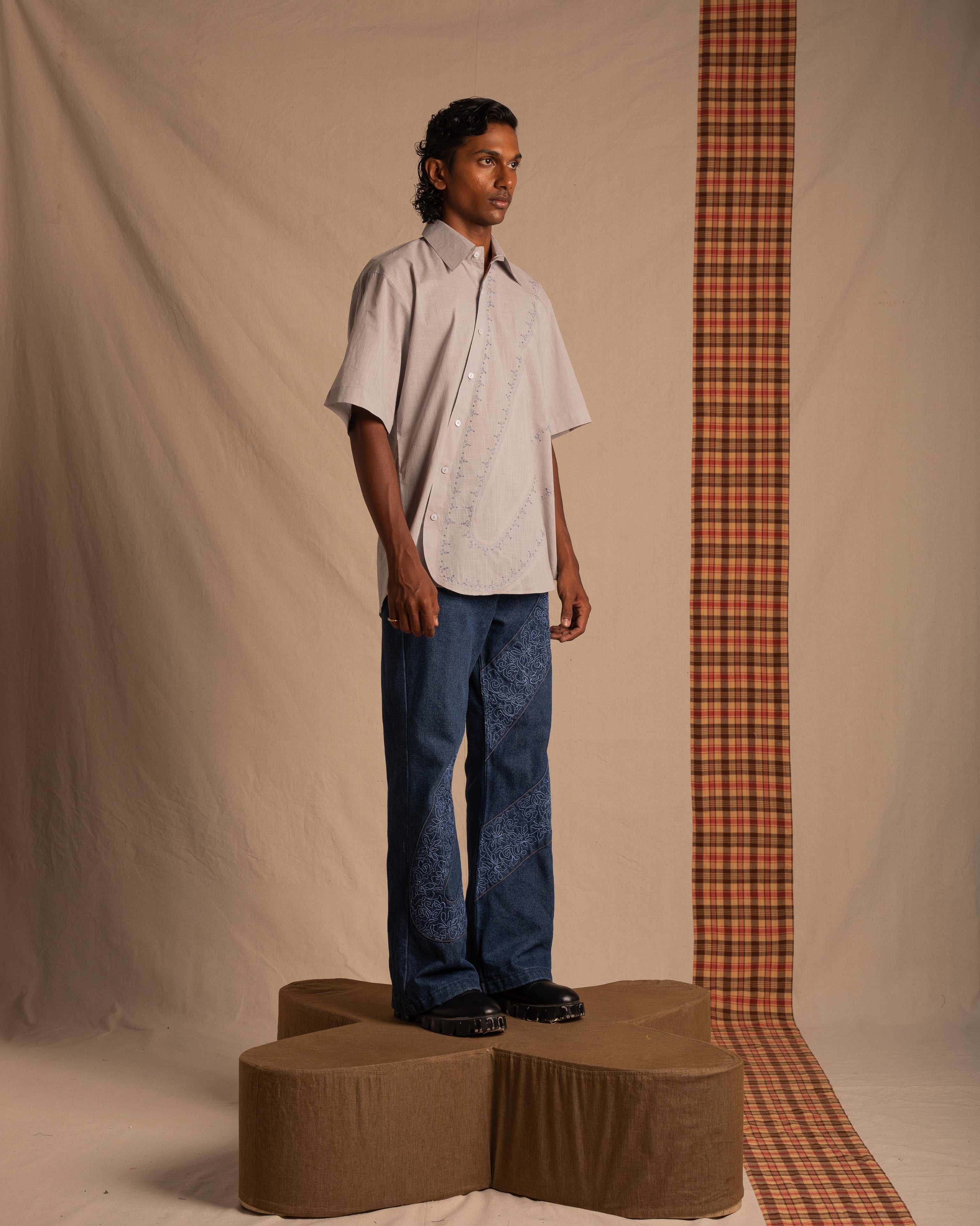Man wearing oversized short-sleeve shirt and blue designer jeans, standing on platform in studio.