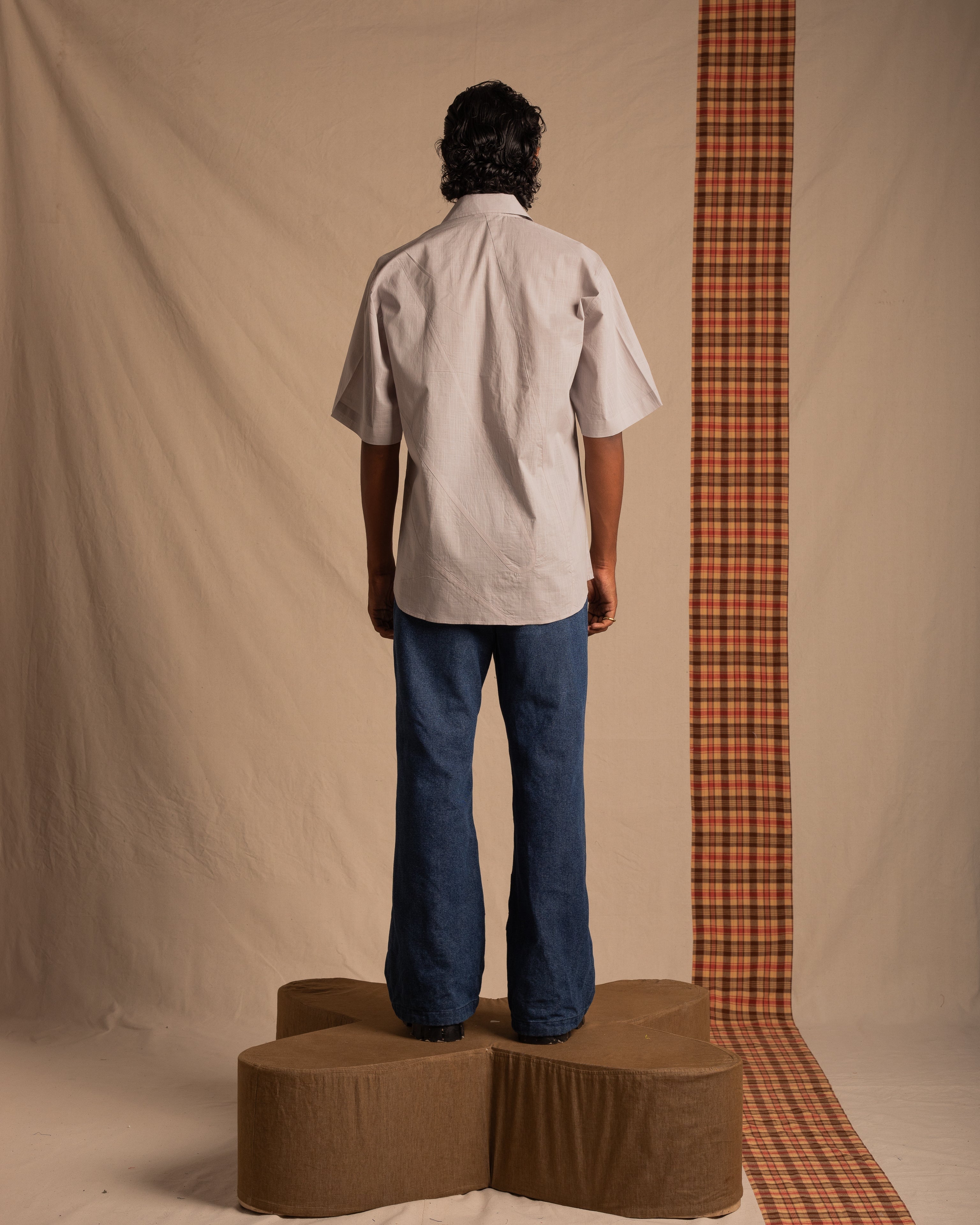 Man in short sleeve shirt and wide leg jeans standing on platform, neutral studio backdrop