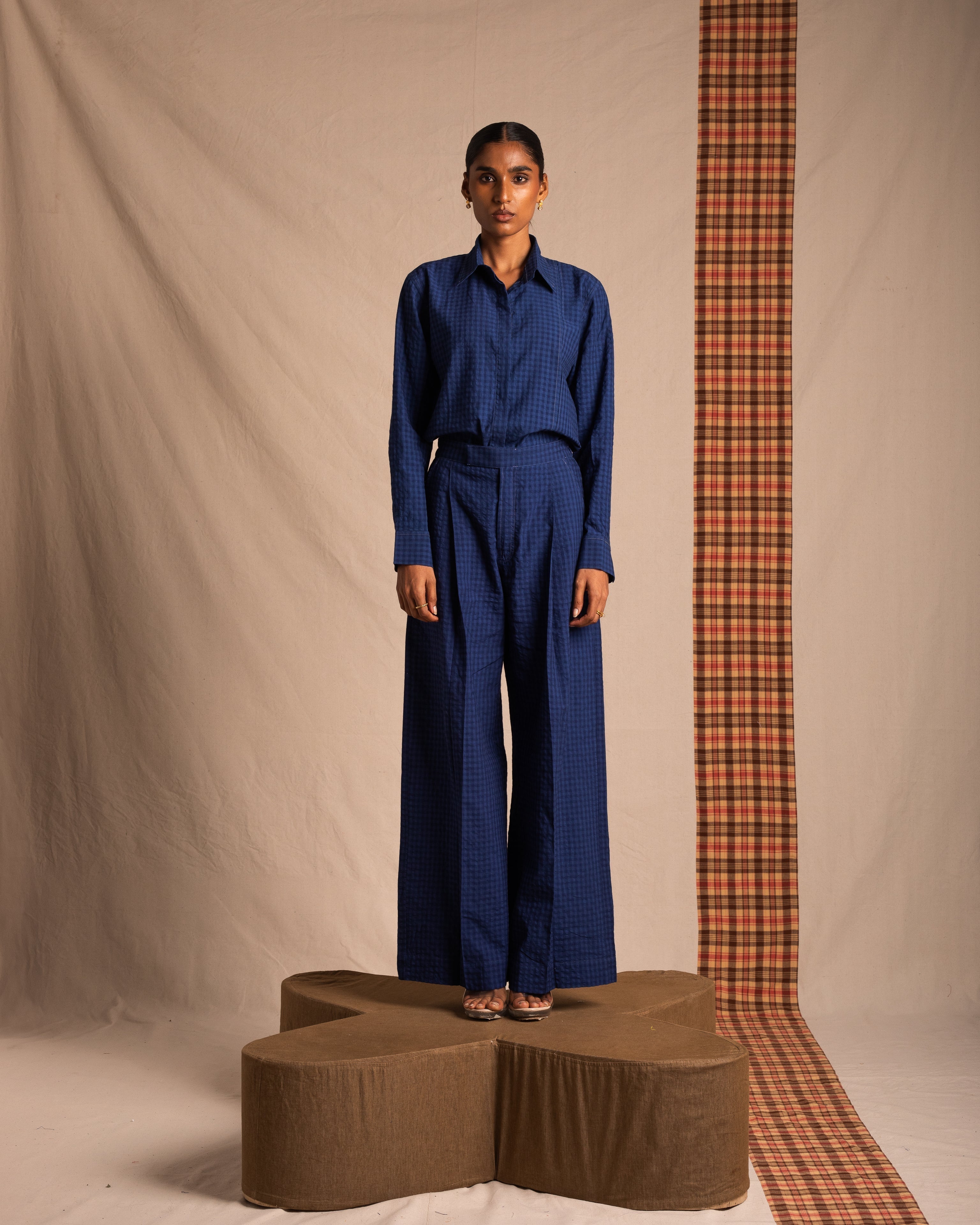 Woman modeling blue checkered streetwear shirt and wide-leg pants on neutral backdrop