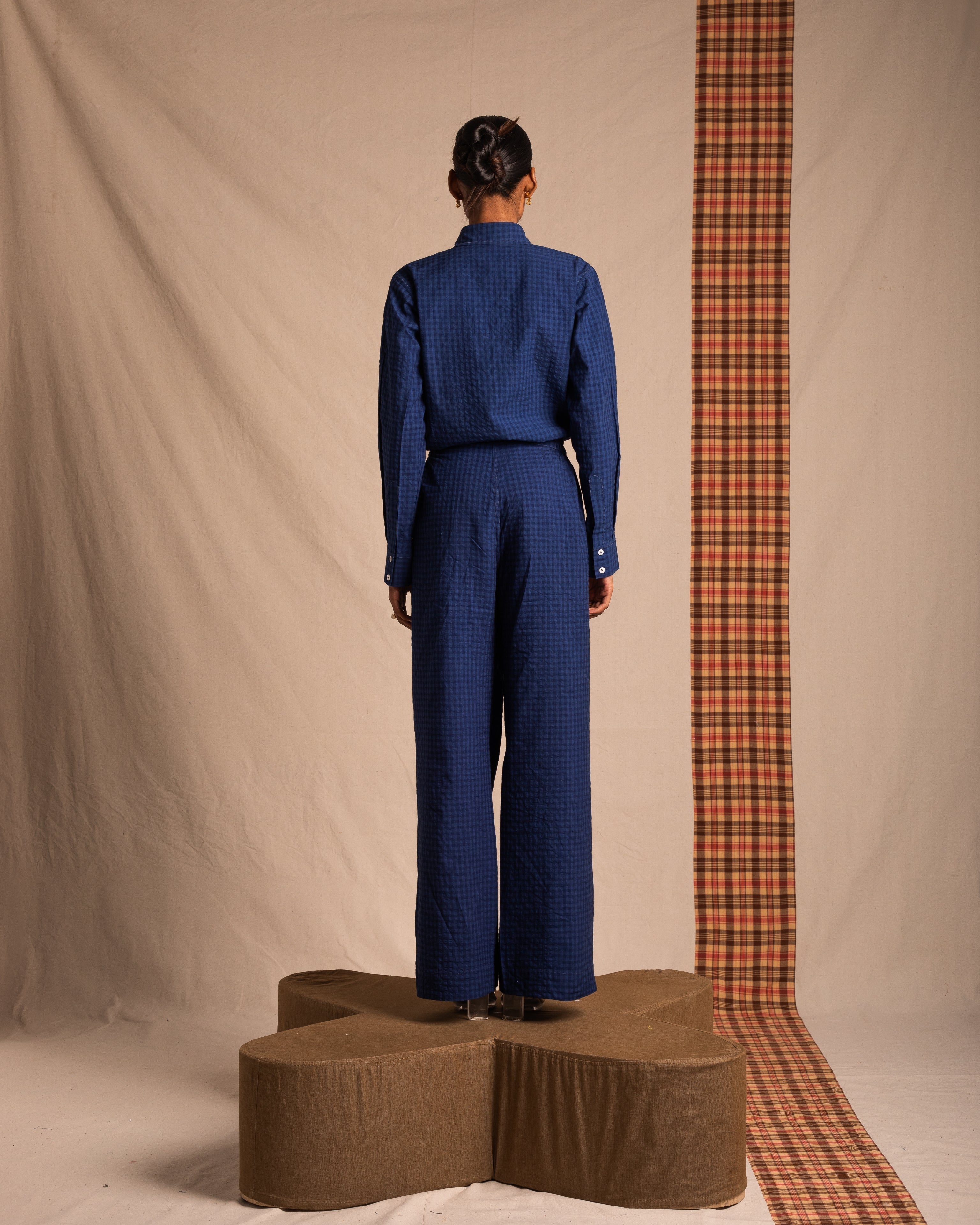 Woman in blue textured pants and shirt, standing on a platform against neutral backdrop