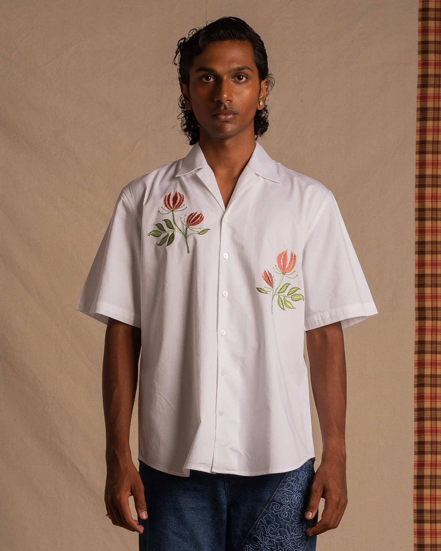 Man wearing a white short-sleeve button-up shirt with floral embroidery and blue jeans