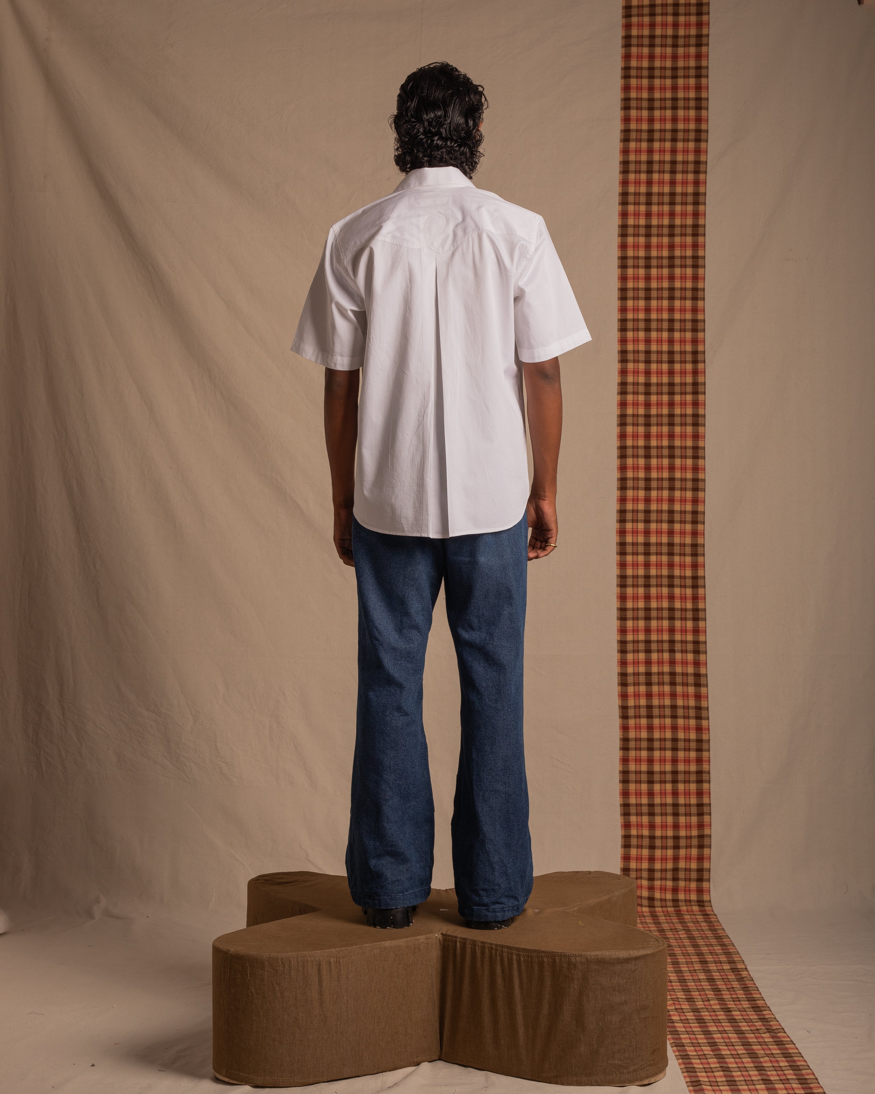 Man modeling streetwear, white short sleeve shirt, blue jeans, neutral studio backdrop