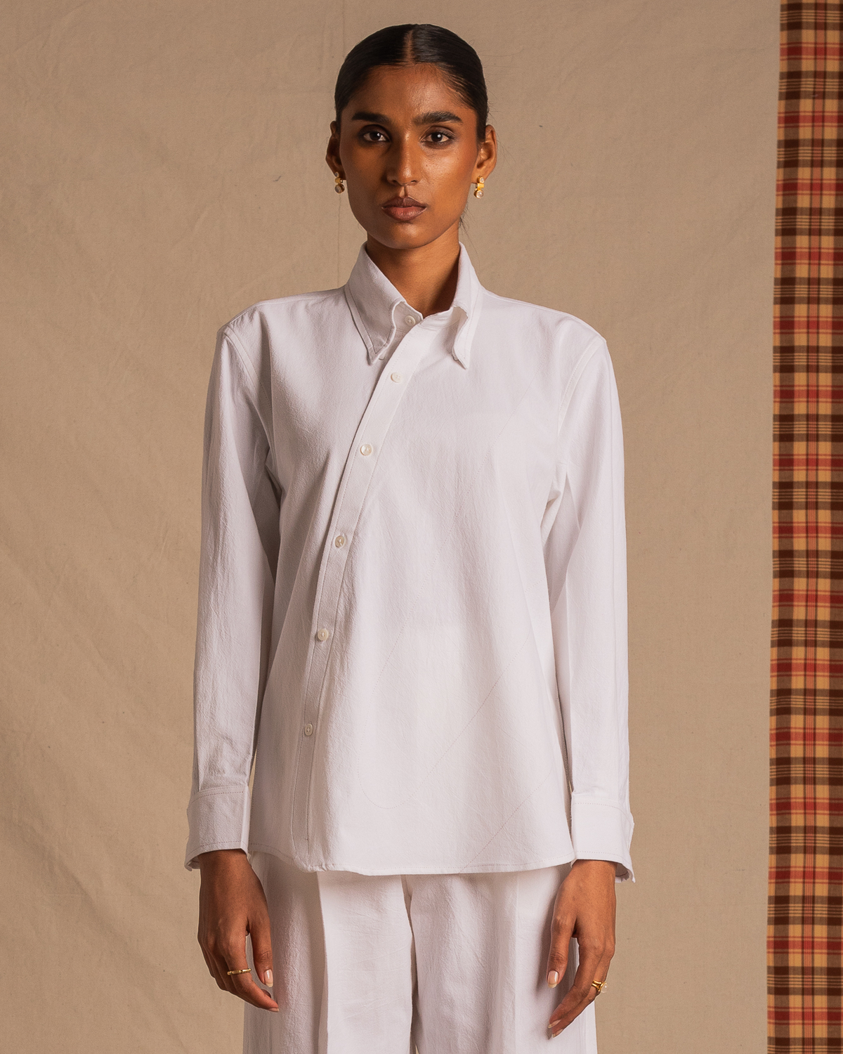 Woman wearing a white asymmetrical button-up shirt and matching pants, minimalist setting