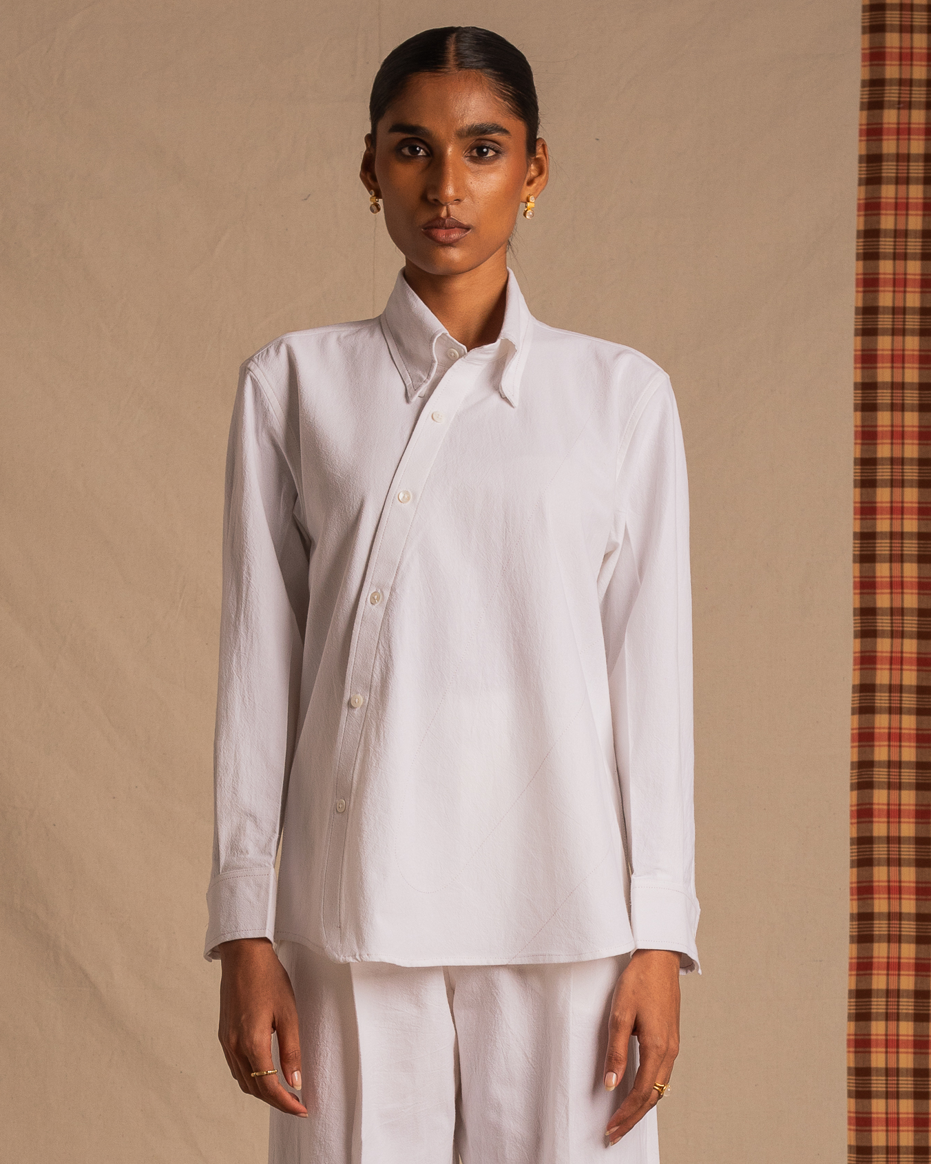 Woman wearing asymmetric white button-up shirt and matching pants, minimalist background