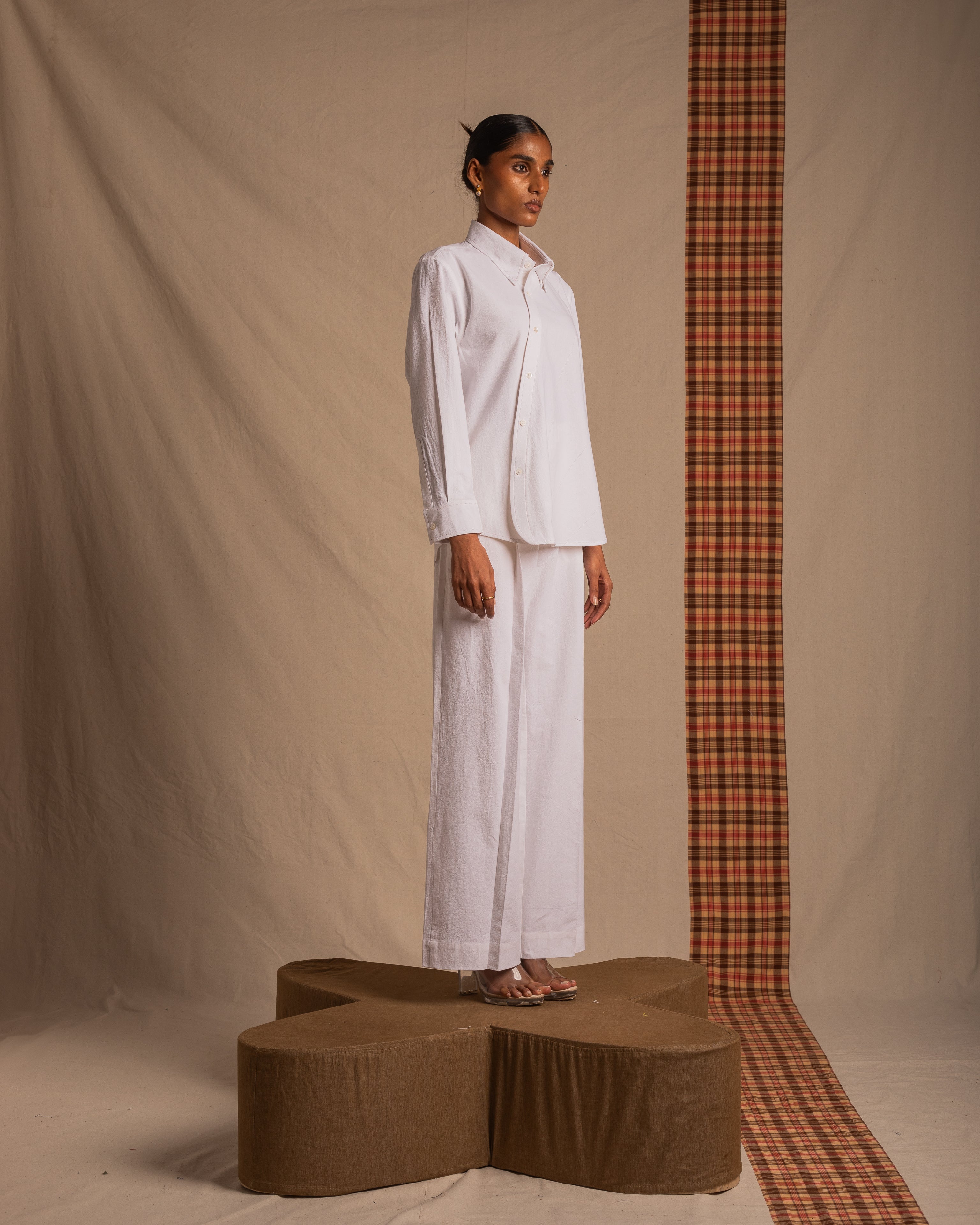 Woman modeling minimalist white button-up shirt and wide-leg pants in a studio with beige backdrop