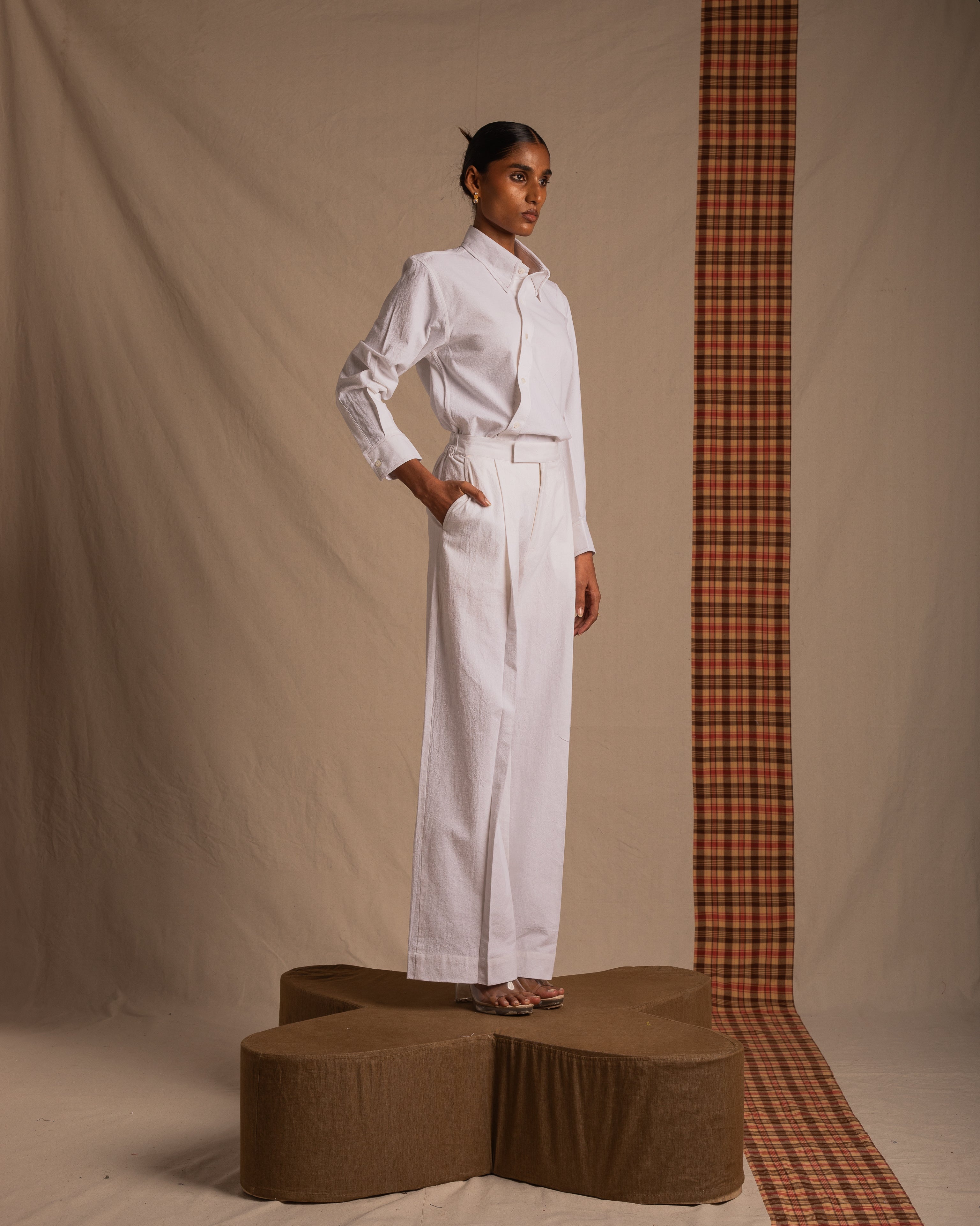 Woman modeling white button-up shirt and wide-leg pants, standing on platform, neutral backdrop